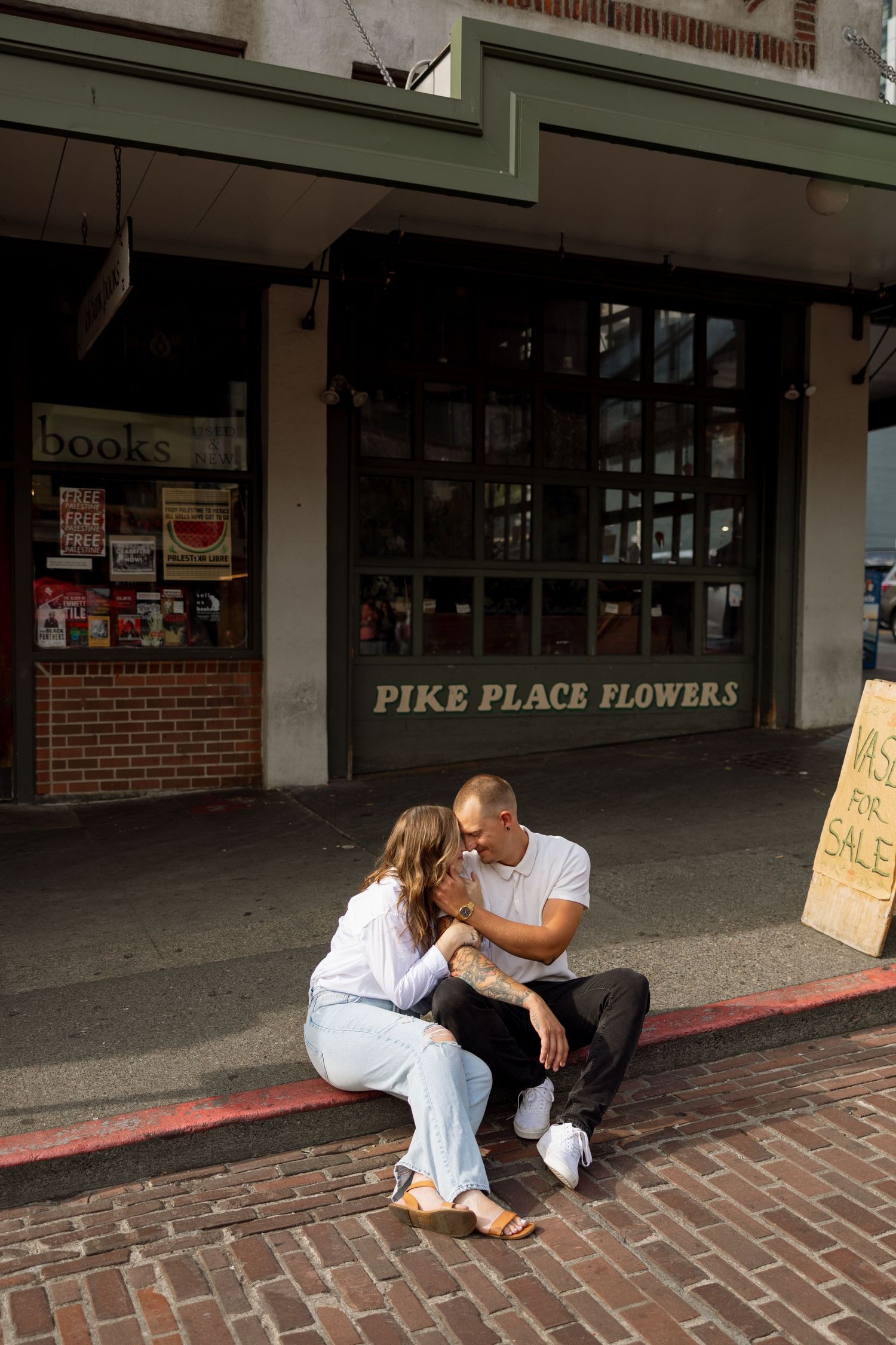 Couple sharing an intimate moment on a brick sidewalk outside Pike Place Flowers shop.