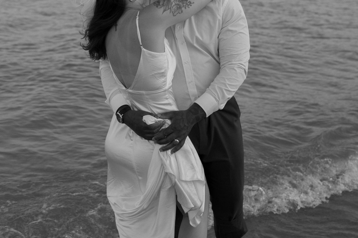 An intimate black and white portrait of a couple embracing by the sea.