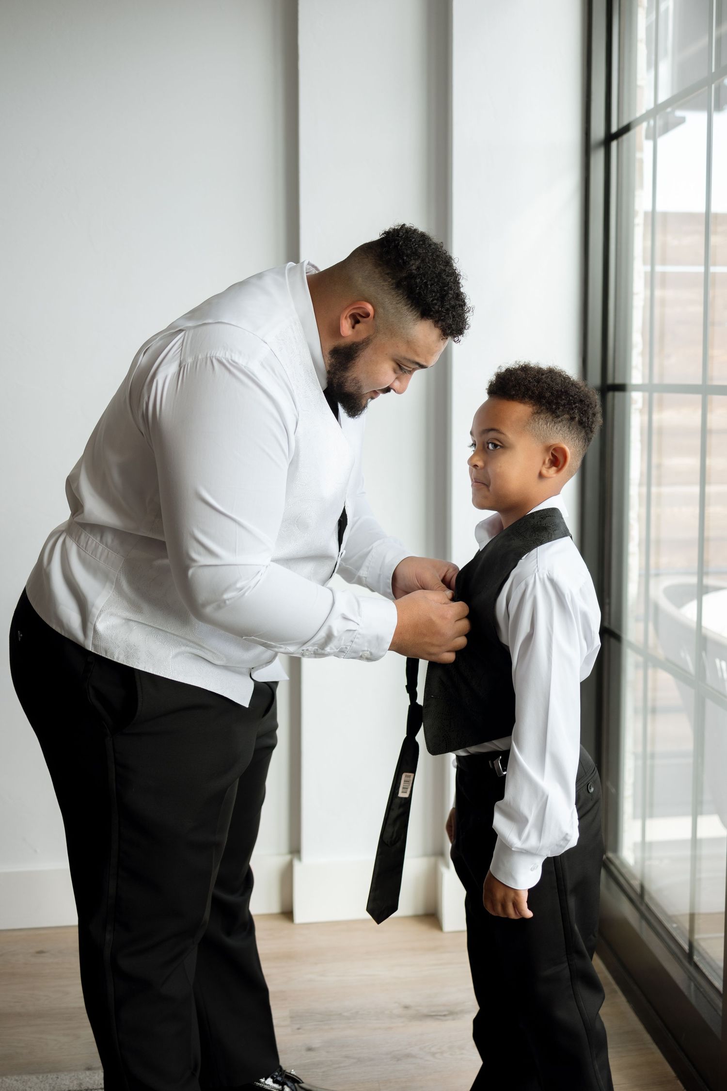 A tender moment as an adult helps adjust a child's tie near a bright window.