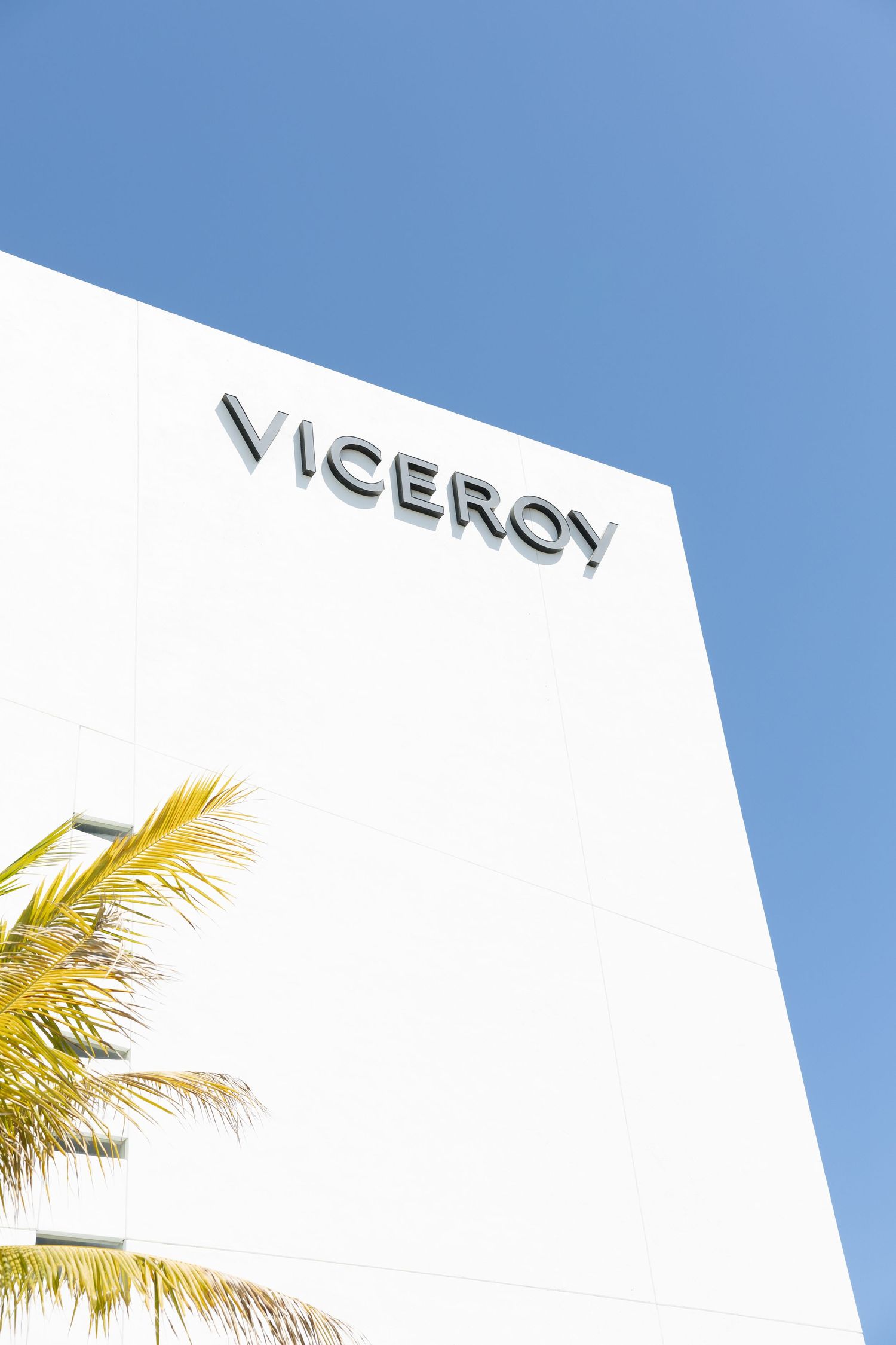 The modern white exterior of the Viceroy hotel building against a clear blue sky with palm tree fronds visible.