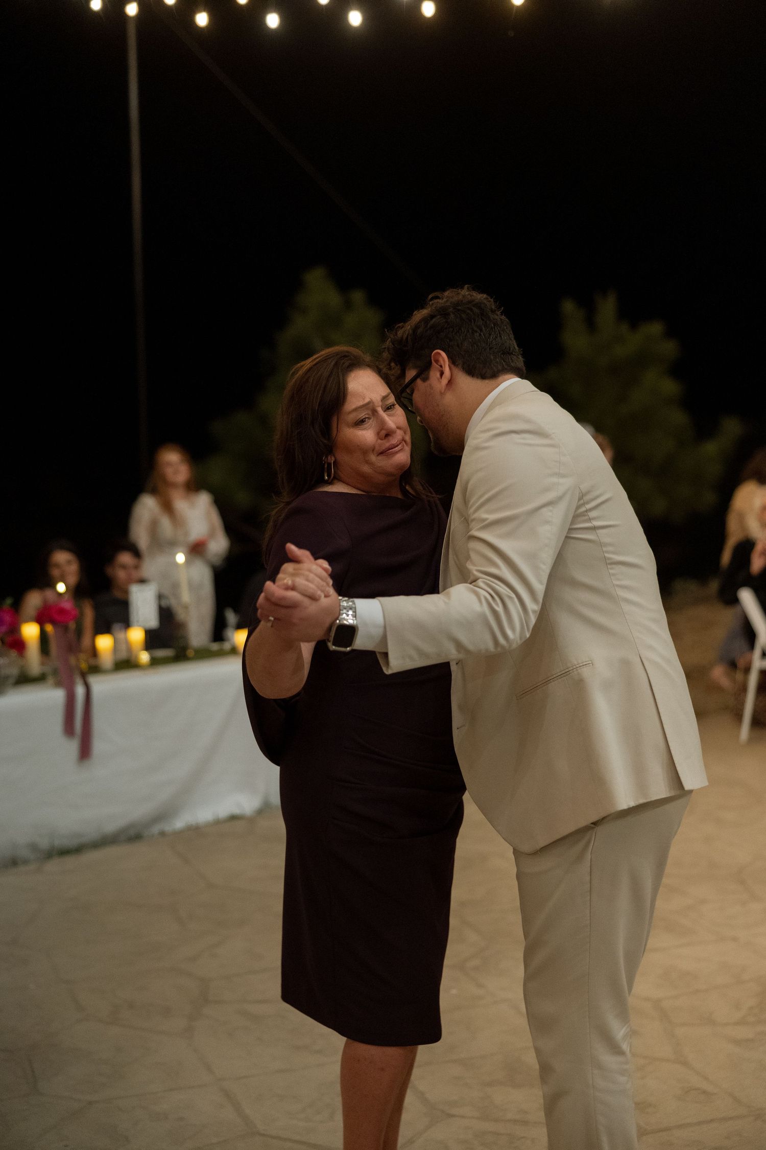 A tender dance moment captured under twinkling outdoor lights at an evening wedding reception.