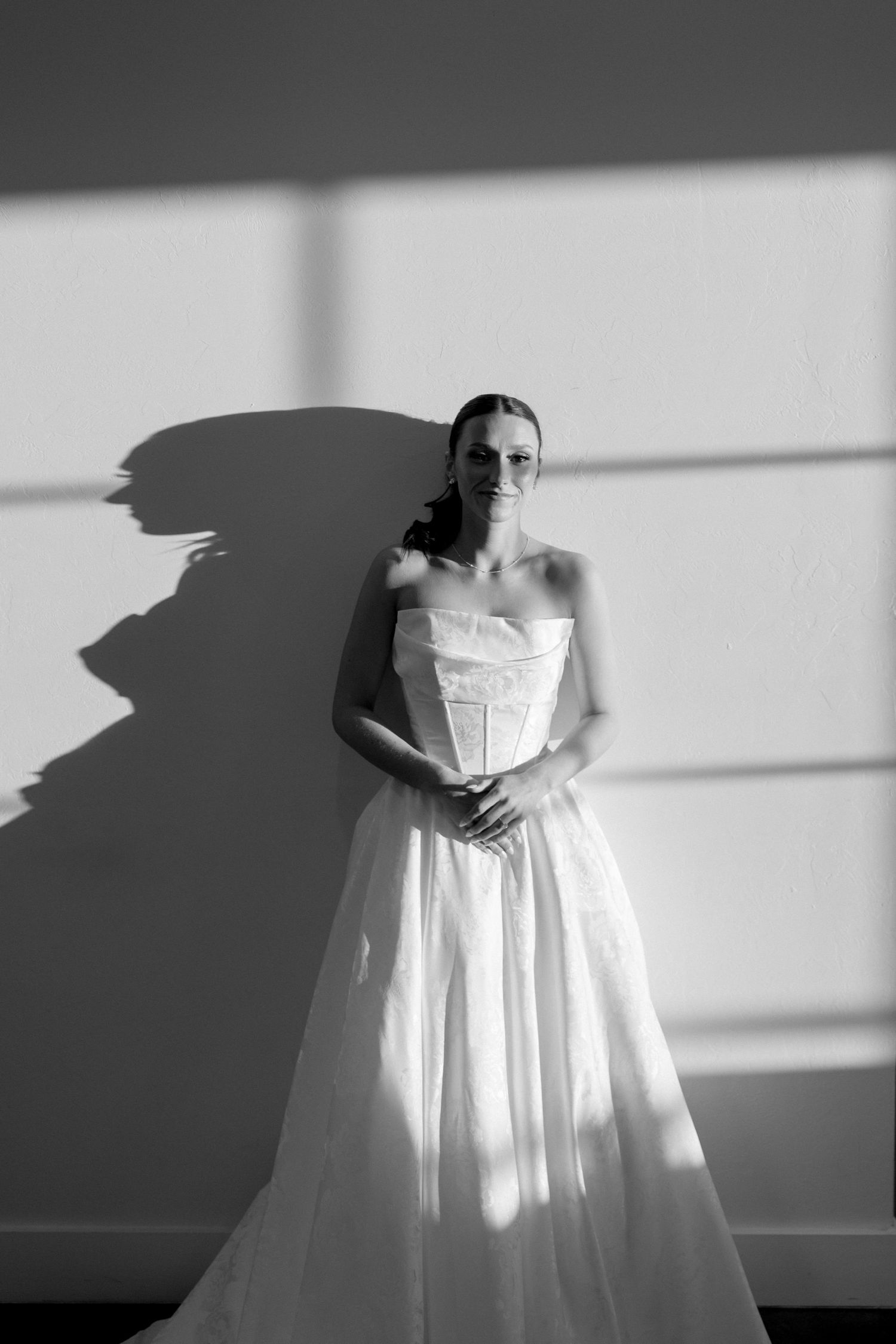 Elegant bridal portrait in black and white showing dramatic window lighting and shadow play.