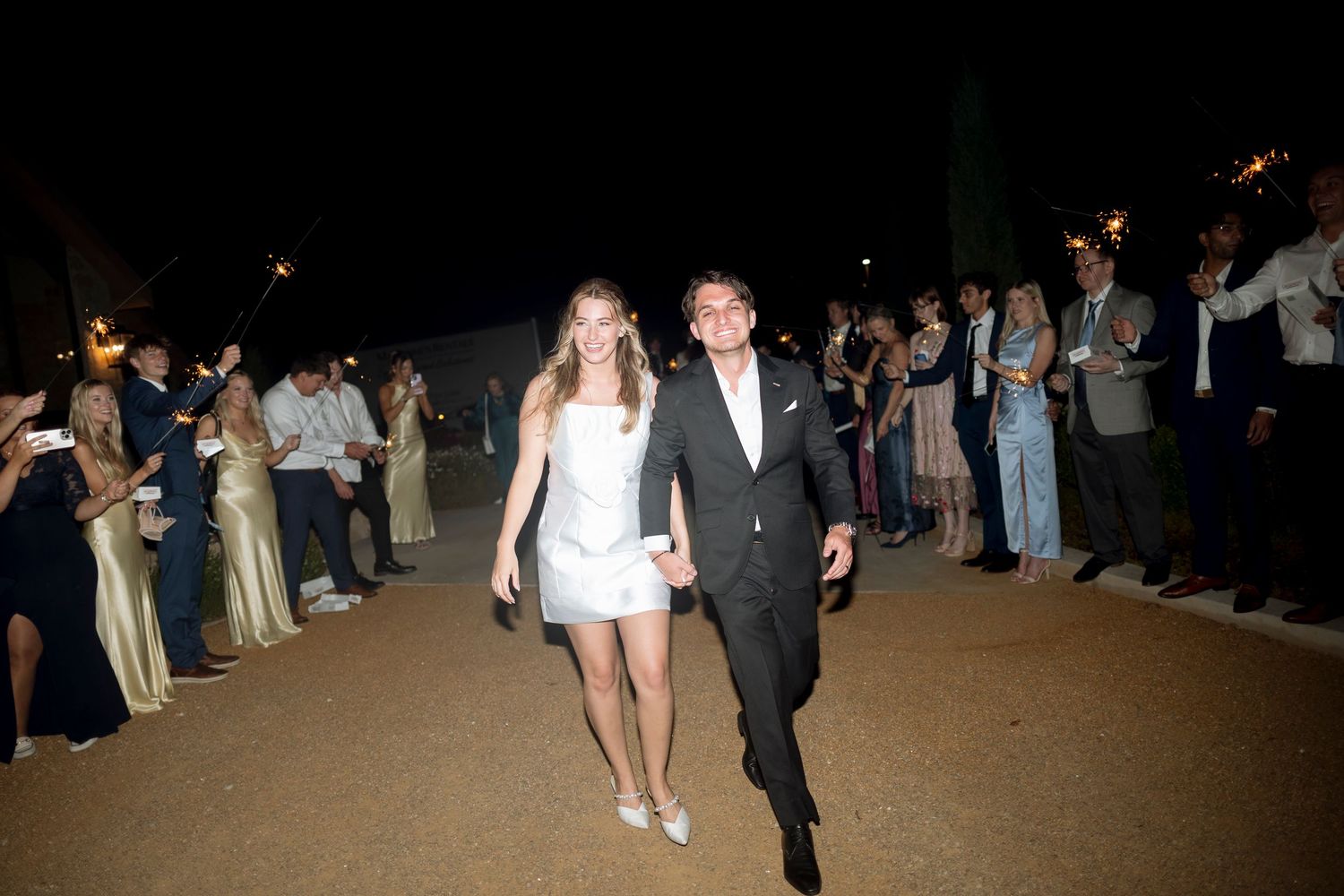Guests in formal attire walking through a dimly lit venue with people lined up along both sides of the walkway.