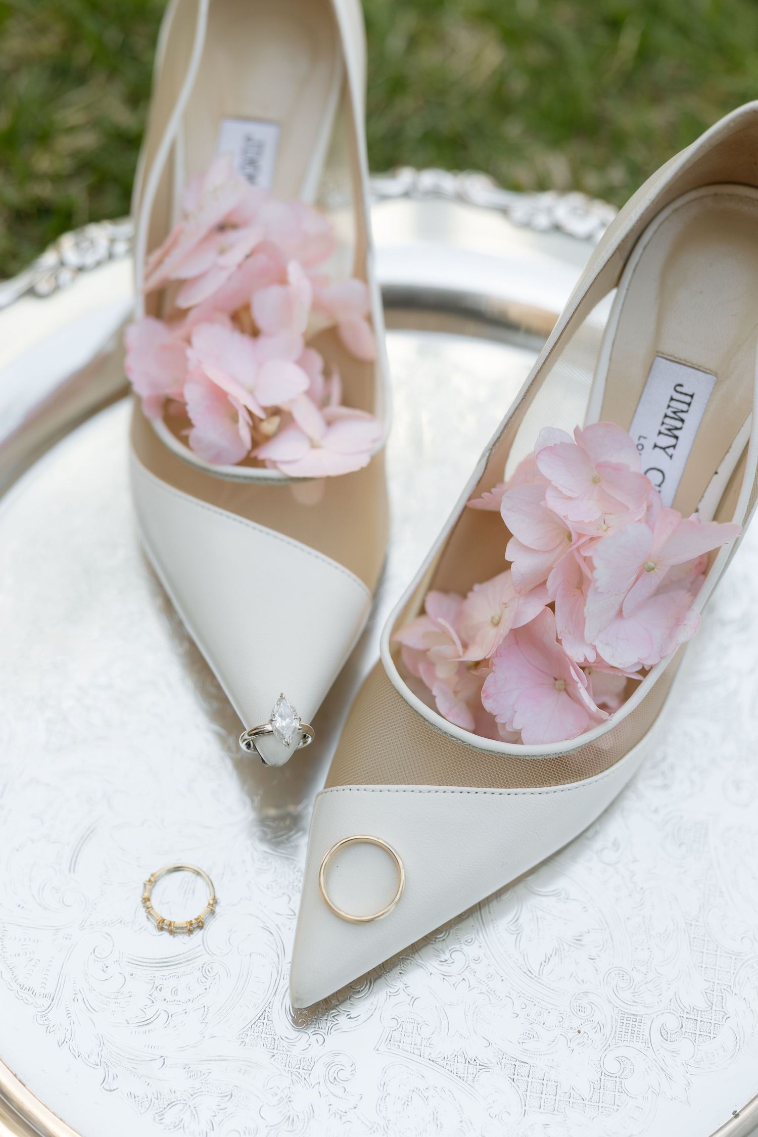 Jimmy Choo bridal heels with pink hydrangeas on silver tray with gold wedding bands nearby.