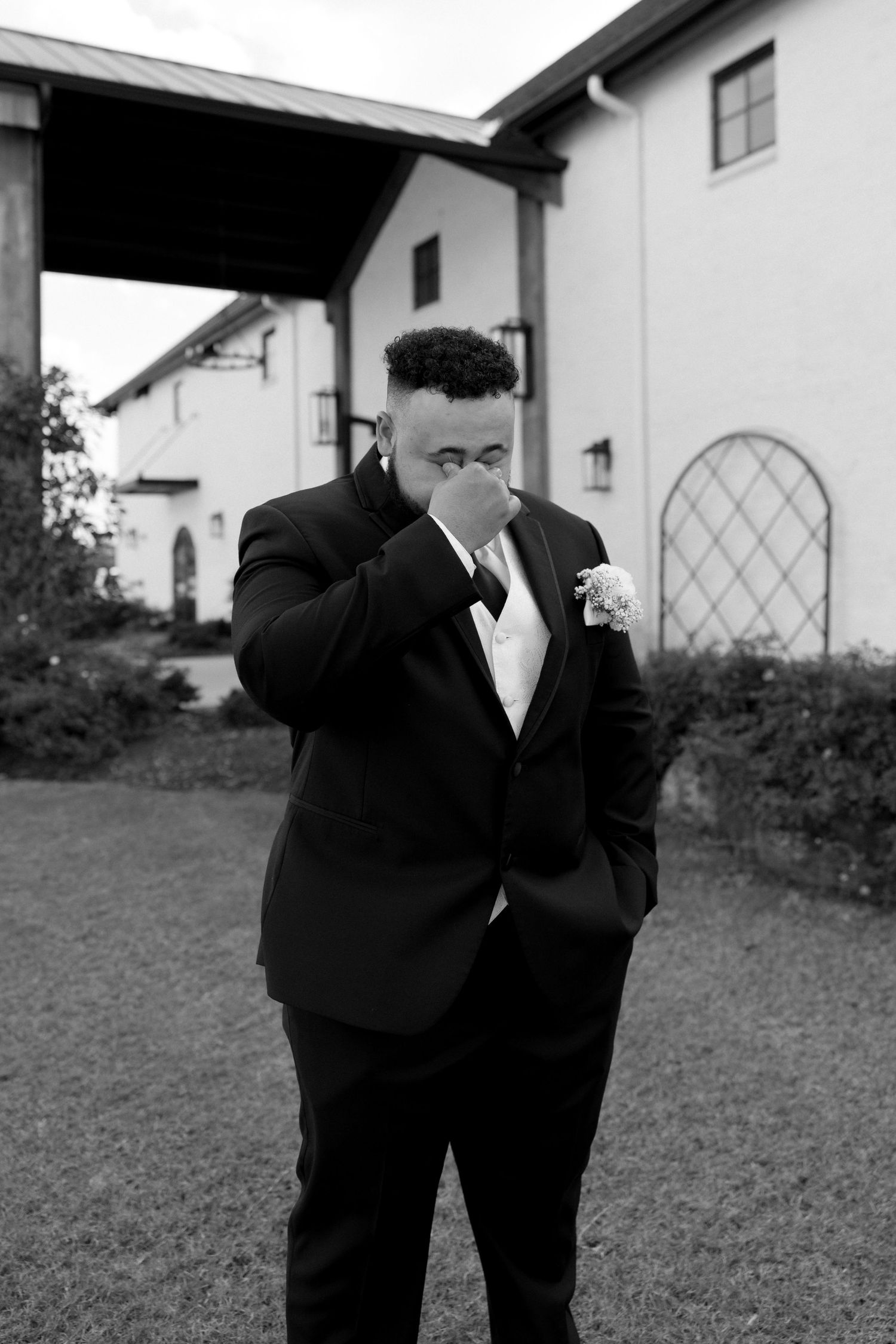 Black and white portrait of emotional groom wiping tears during wedding ceremony.