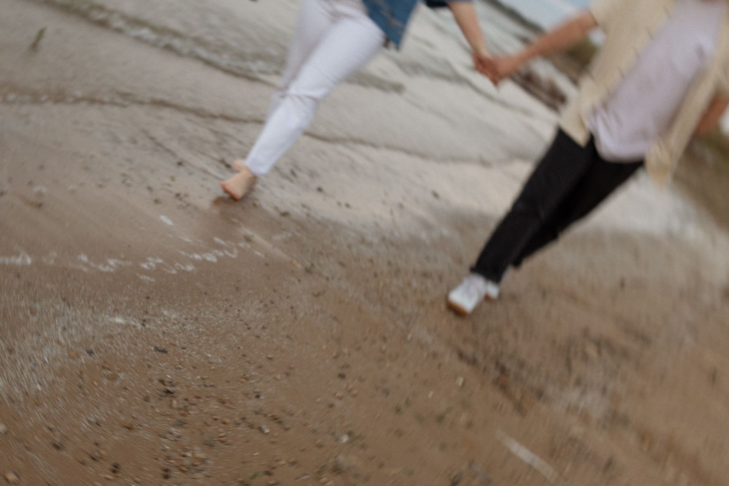 Blurred motion shot of feet walking along a sandy beach shoreline.