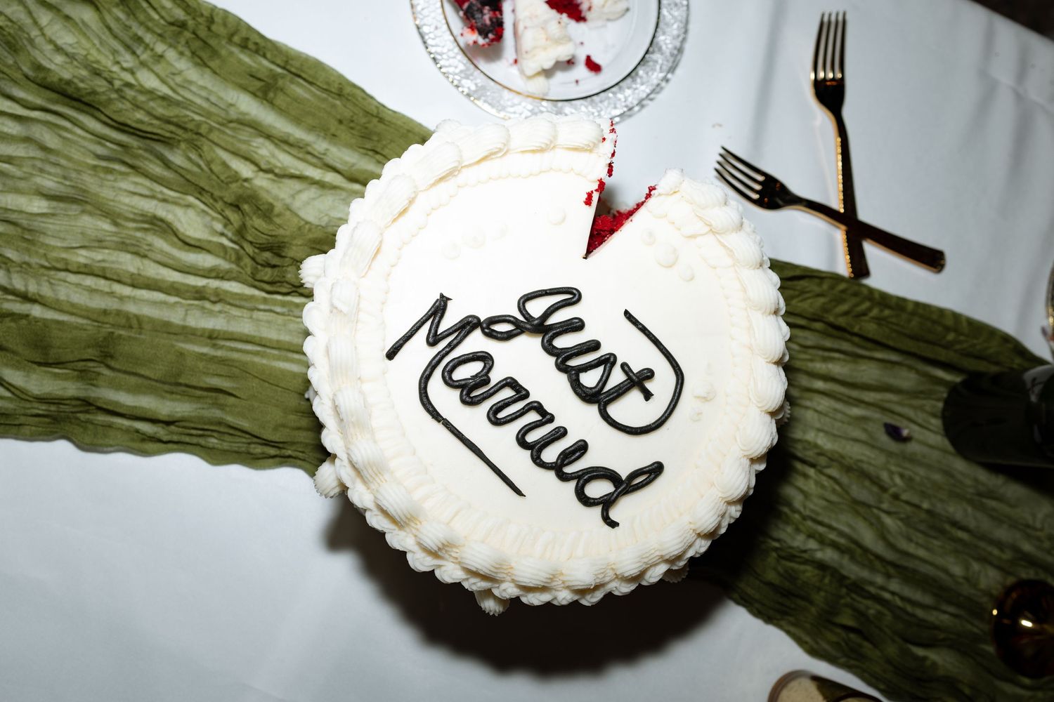 White frosted cake with 'Just Married' written in black icing on green tablecloth.
