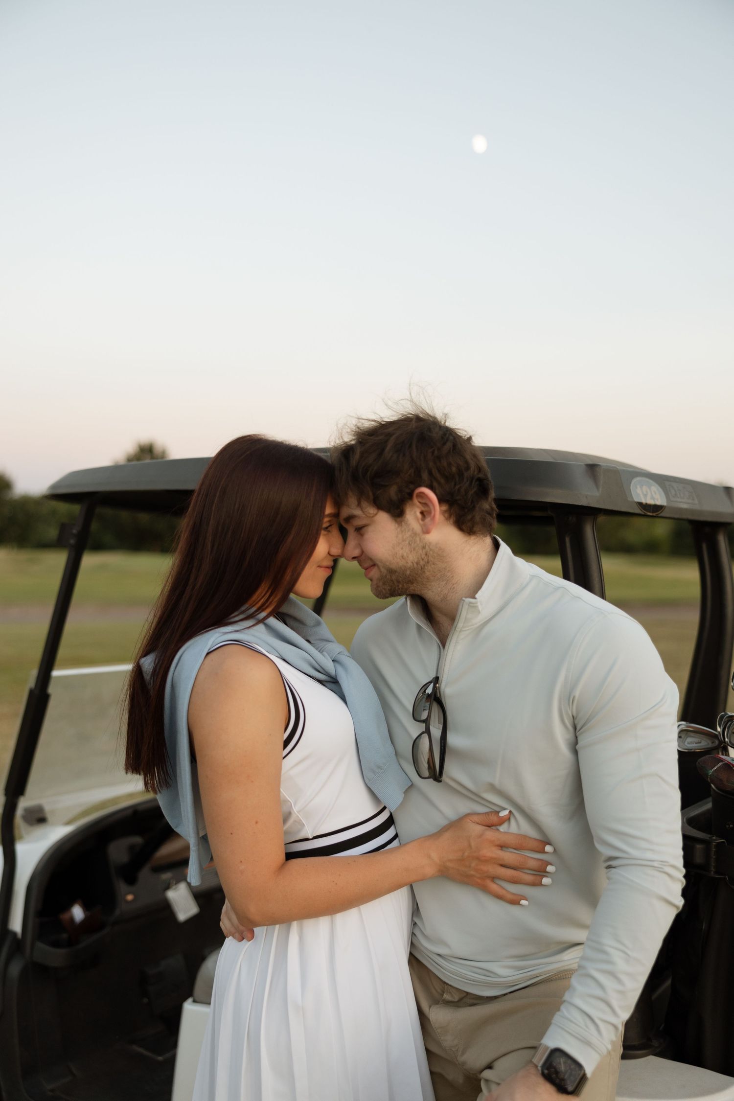 An intimate moment between a couple next to a golf cart at sunset.