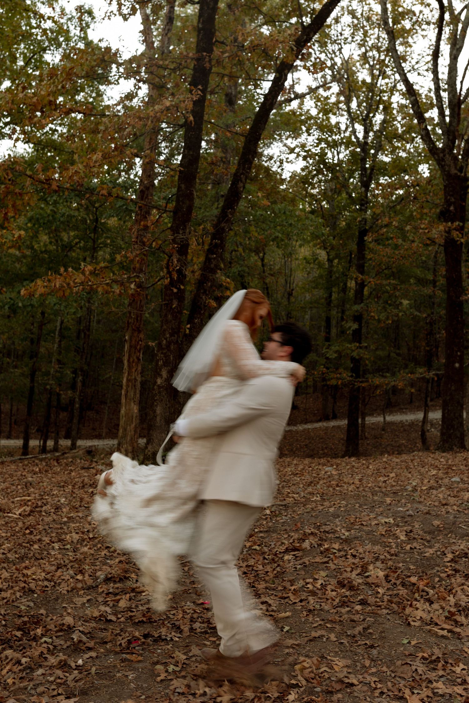 A playful wedding moment captured with the couple spinning in an autumn forest.