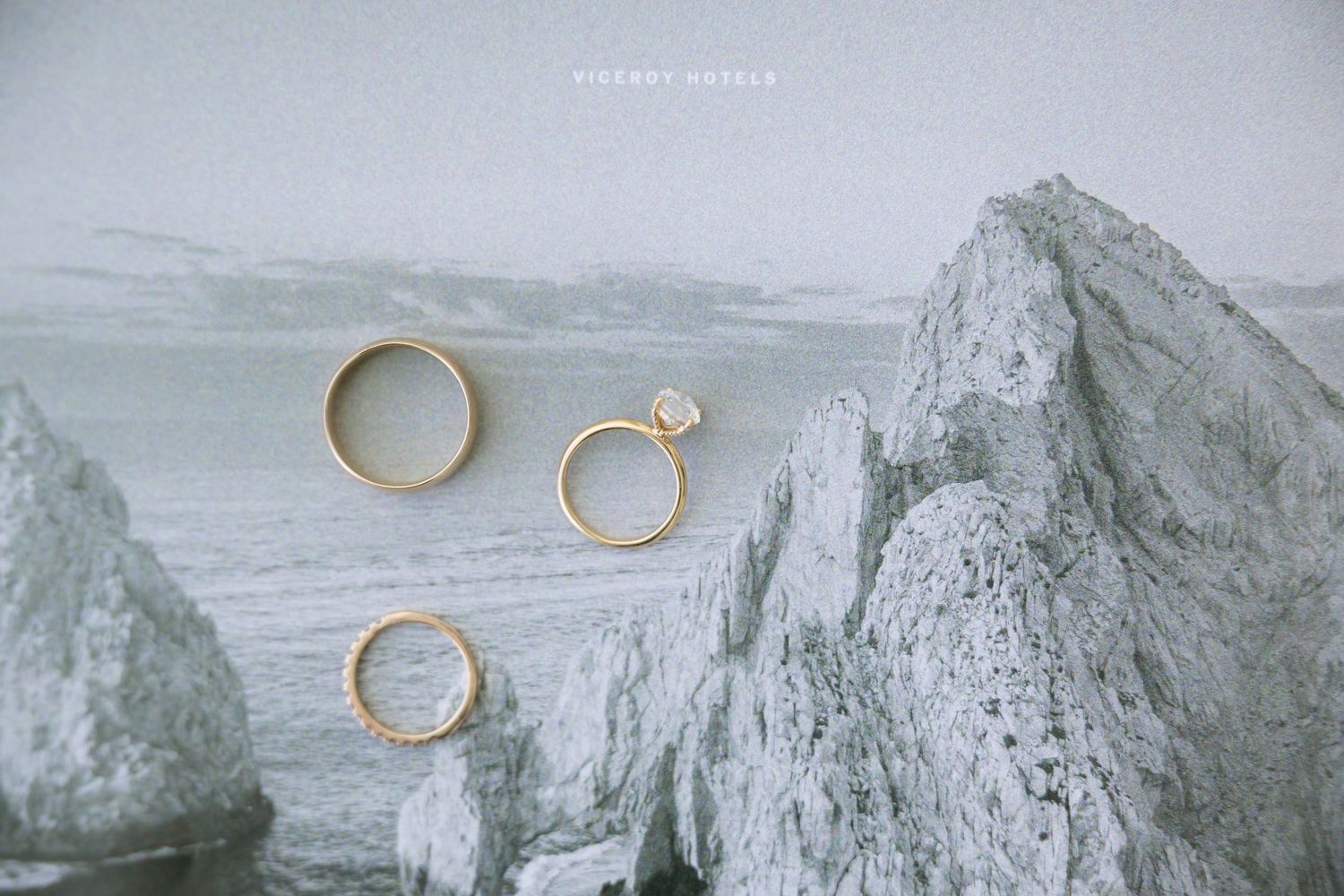 Three gold wedding and engagement rings displayed on rocky mountain landscape art print.