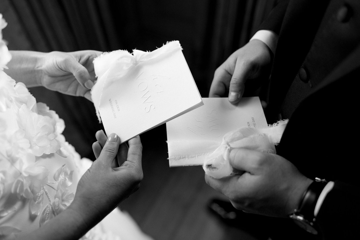 Black and white close-up of bride and groom exchanging handwritten vows during wedding ceremony.