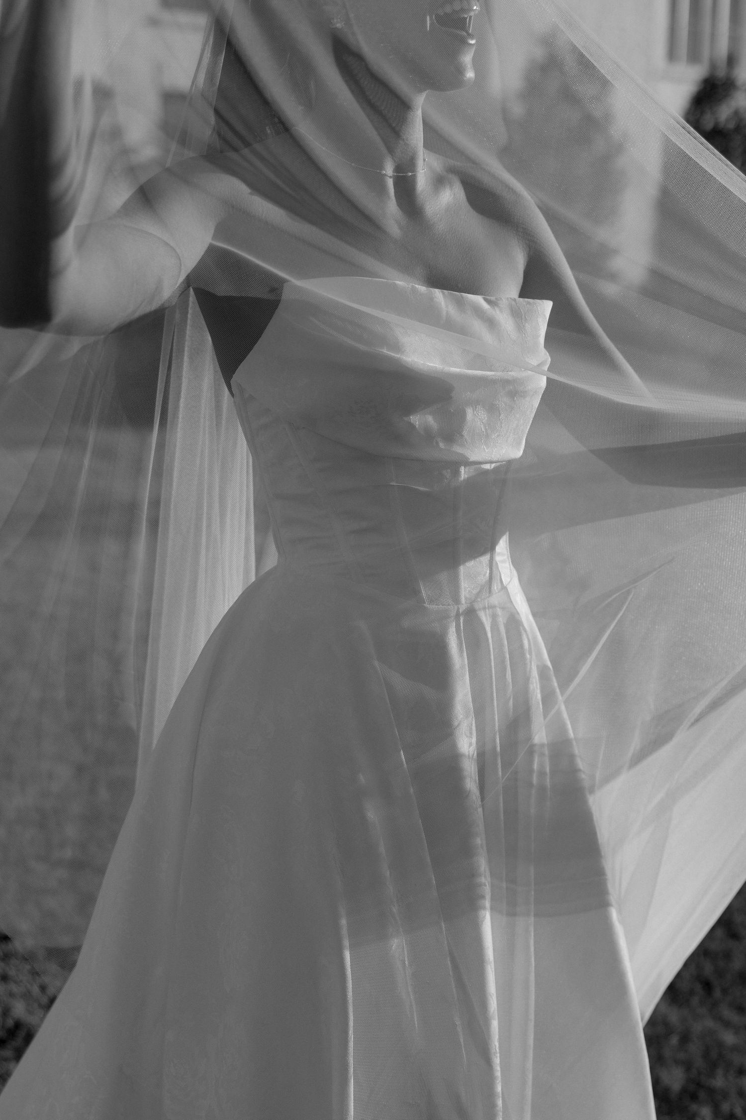 Artistic black and white photo showing details of a strapless wedding dress with flowing veil.
