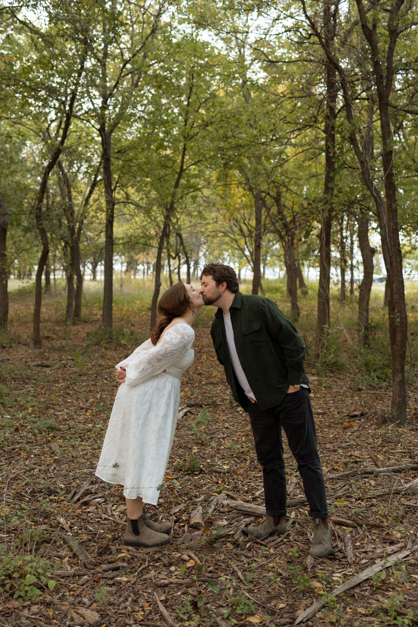 A couple shares a tender kiss among autumn trees in a forest setting.