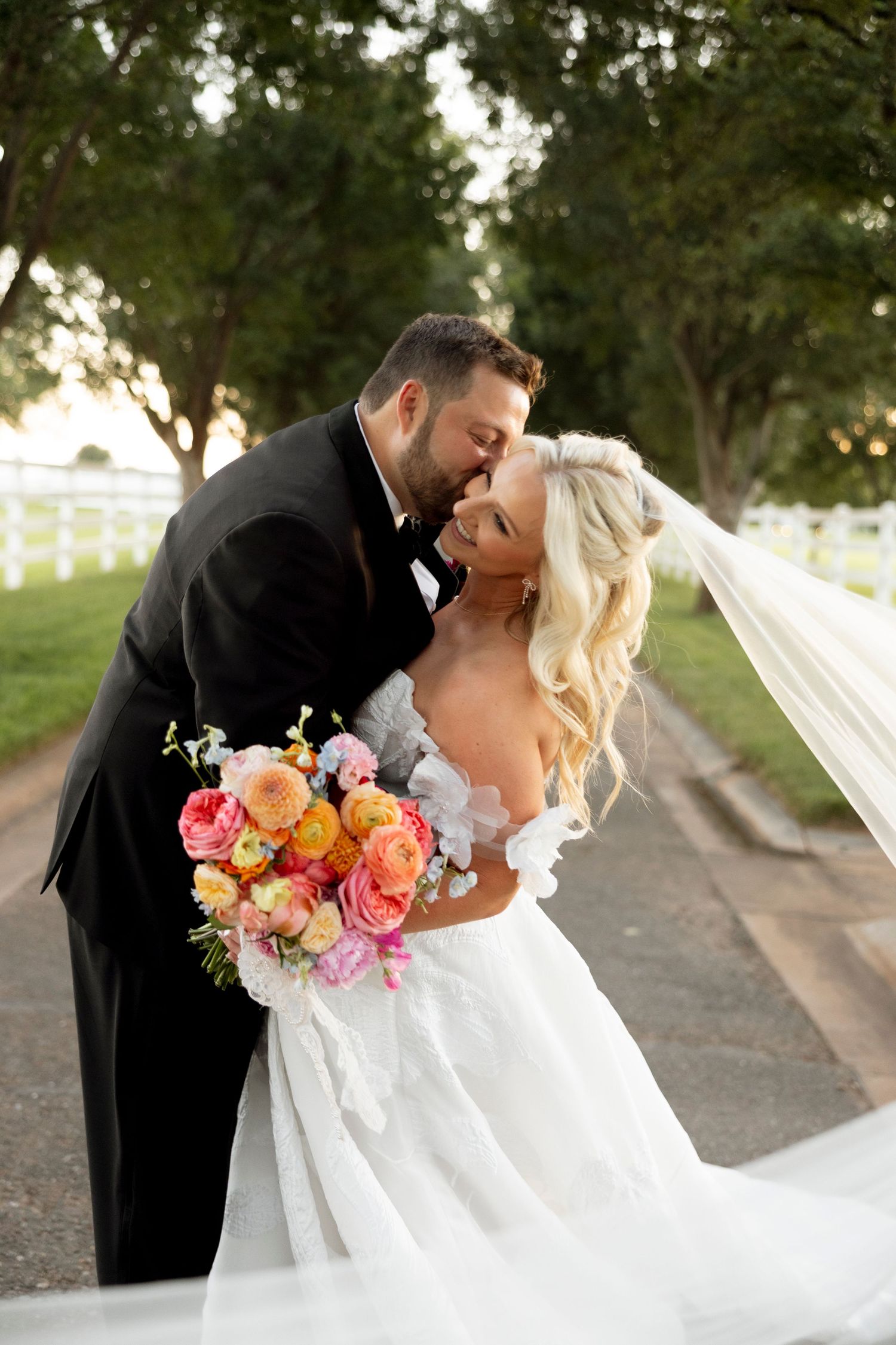 Couple embraces during sunset wedding photos with bride holding vibrant floral bouquet.