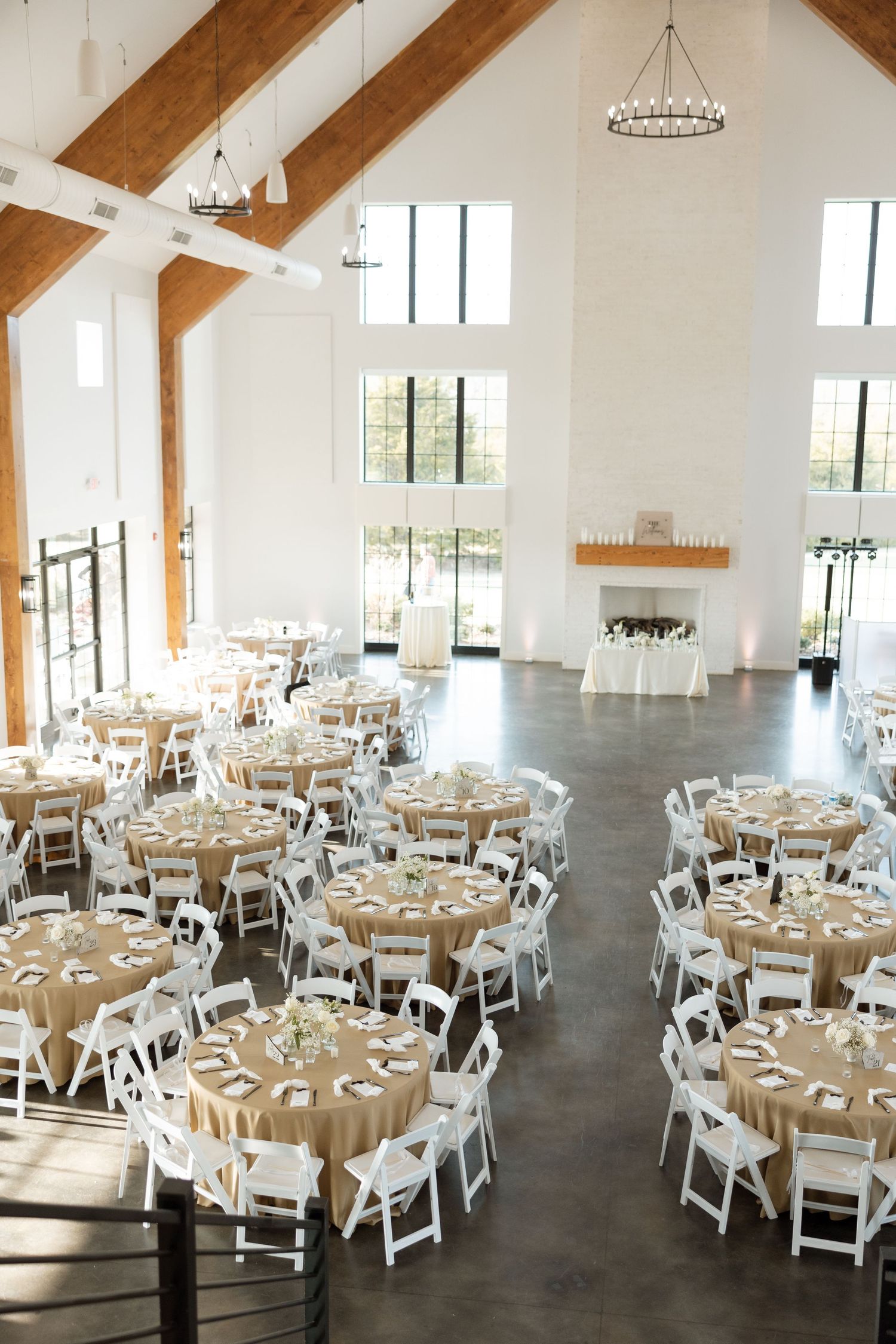 Modern wedding venue with high ceilings, wooden beams, and round tables set for reception.
