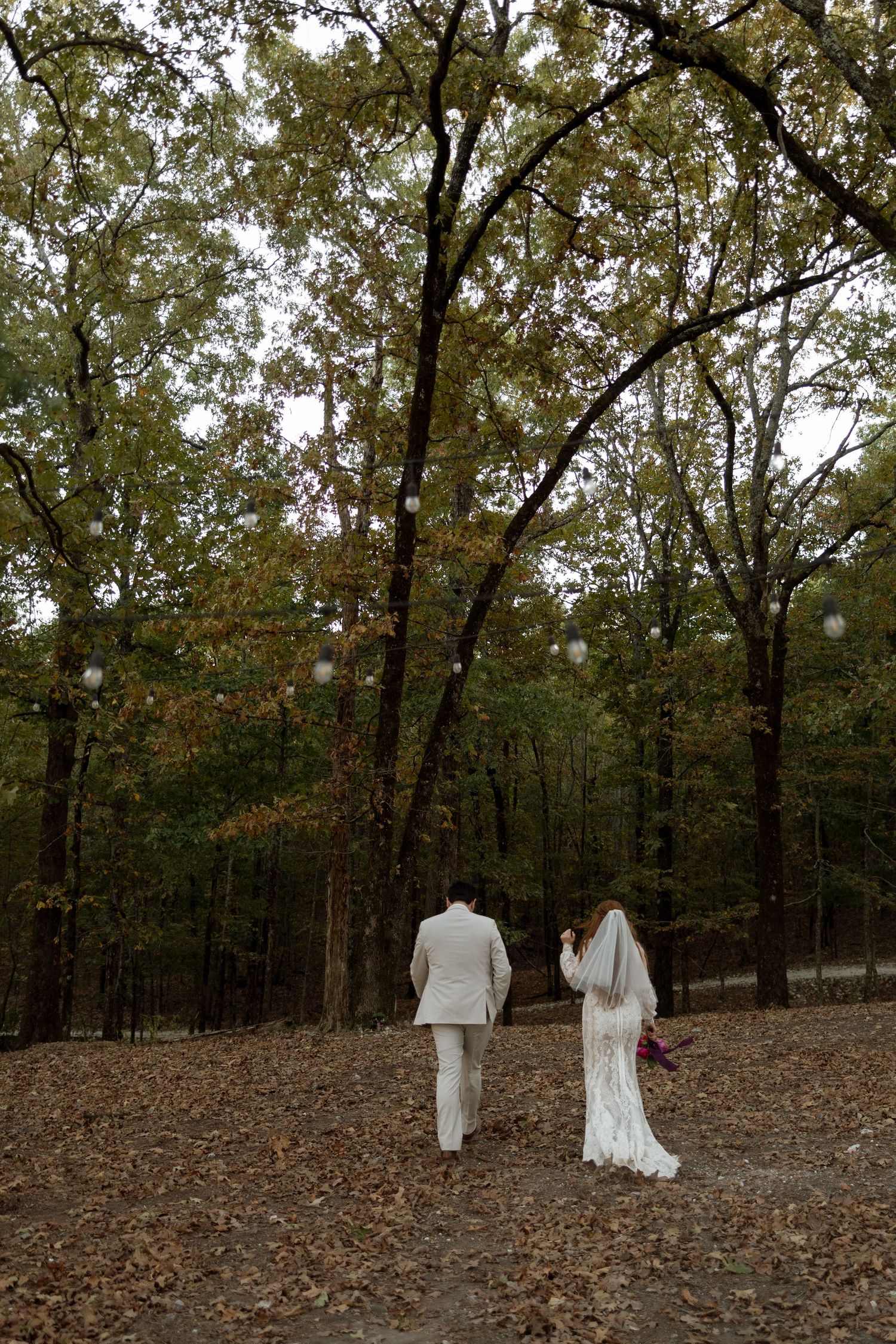 A couple walking hand in hand through an autumn forest path in wedding attire.