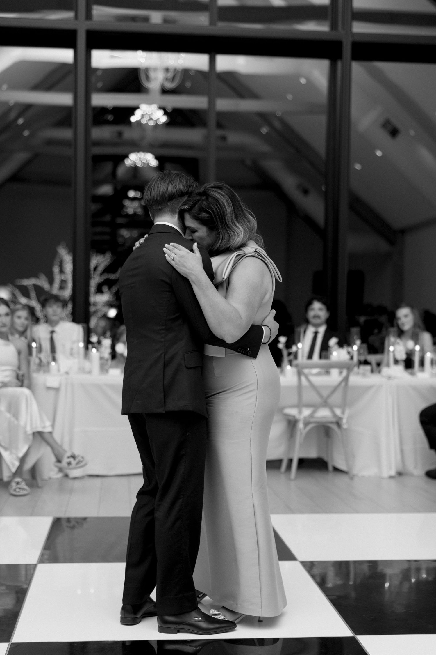 A couple shares their first dance at a wedding reception on a black and white checkered dance floor.