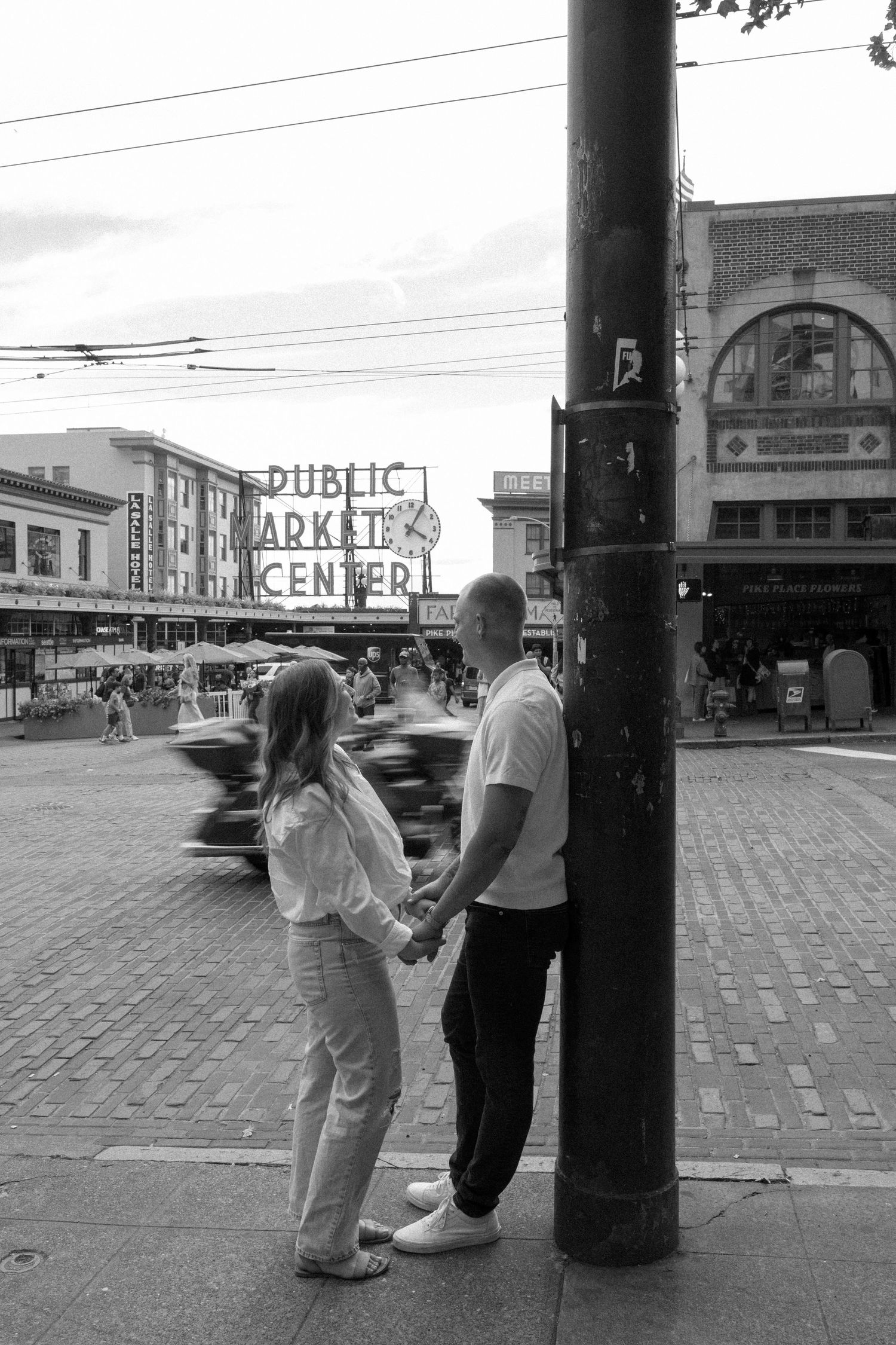 Black and white street scene at Pike Place Market with couple viewing the iconic sign.