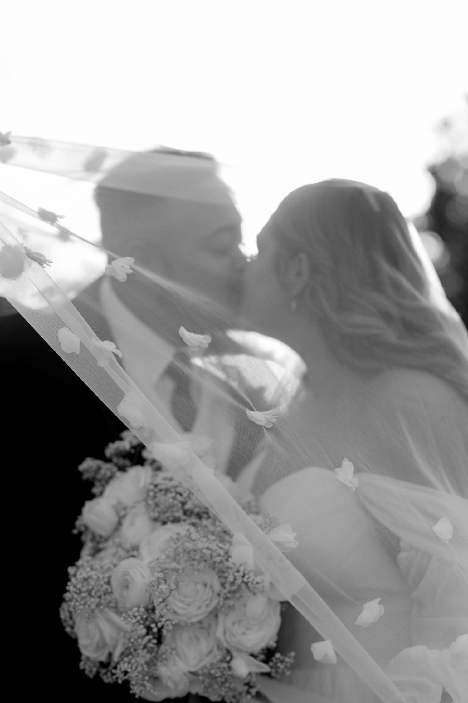 A black and white artistic wedding photo through a veil with bouquet in foreground.