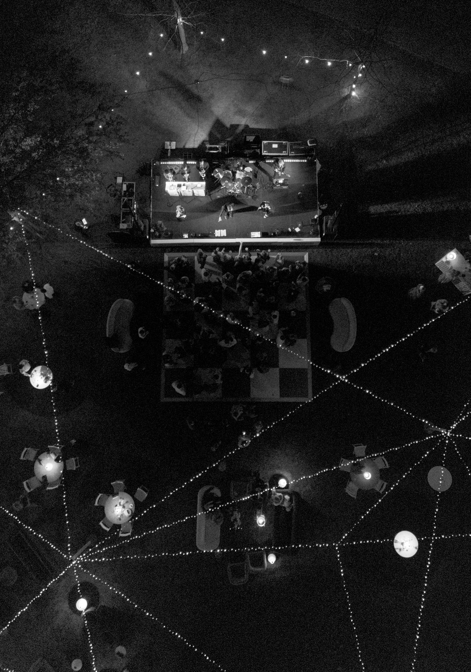 Aerial black and white view of outdoor wedding reception with string lights and illuminated tables.