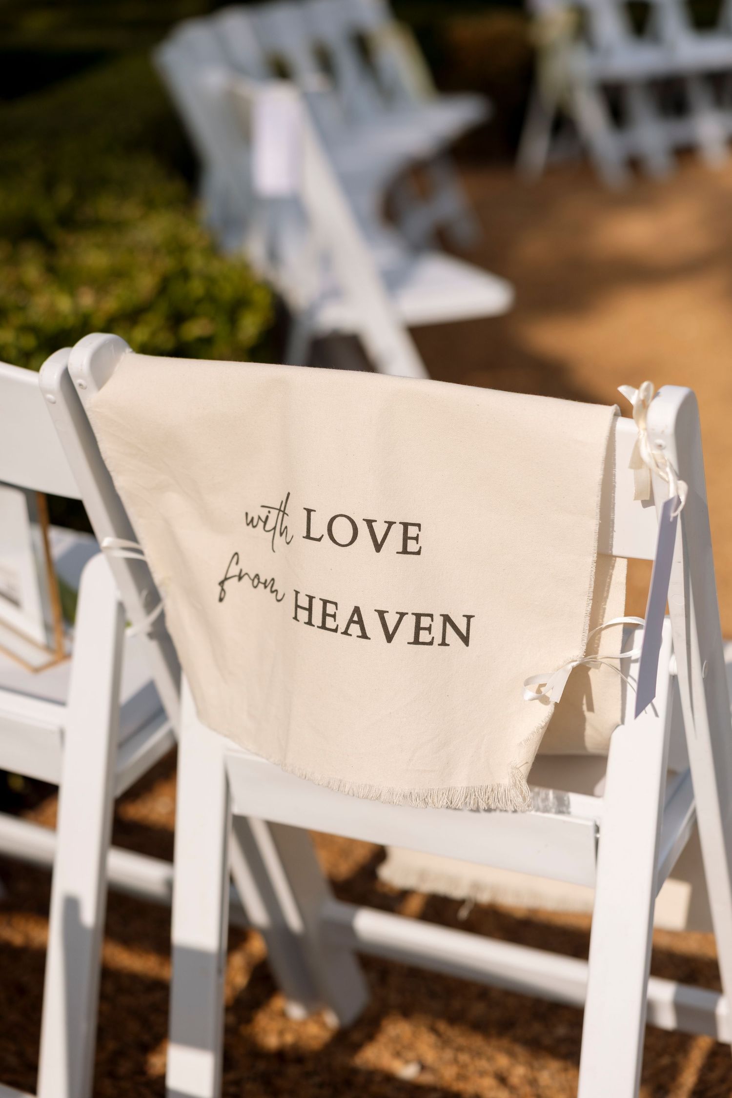White wedding ceremony chair with a cloth sign reading 'with LOVE from HEAVEN' draped over the back.