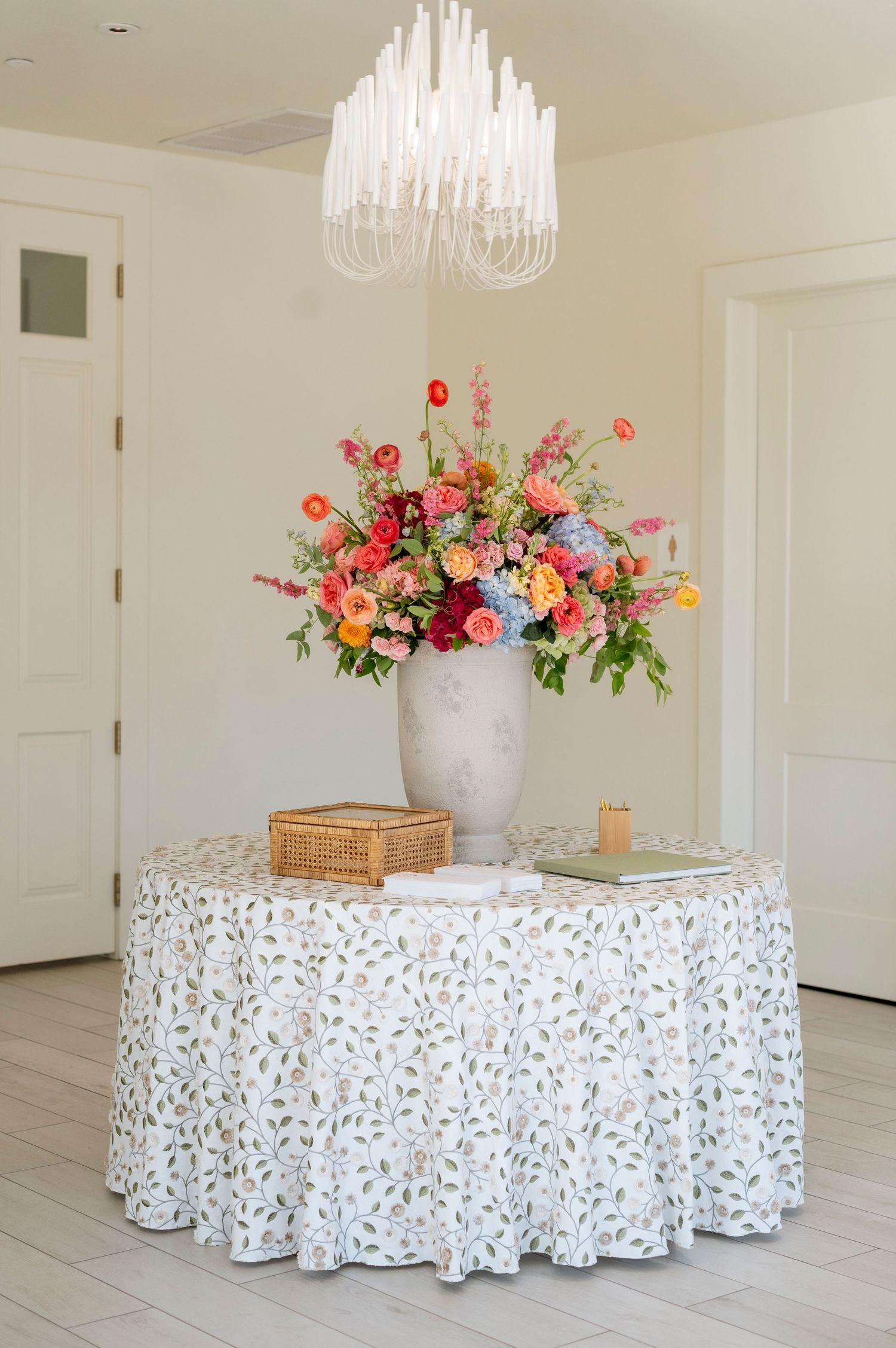 Elegant round tables with floral centerpieces and white patterned tablecloths under crystal chandeliers.