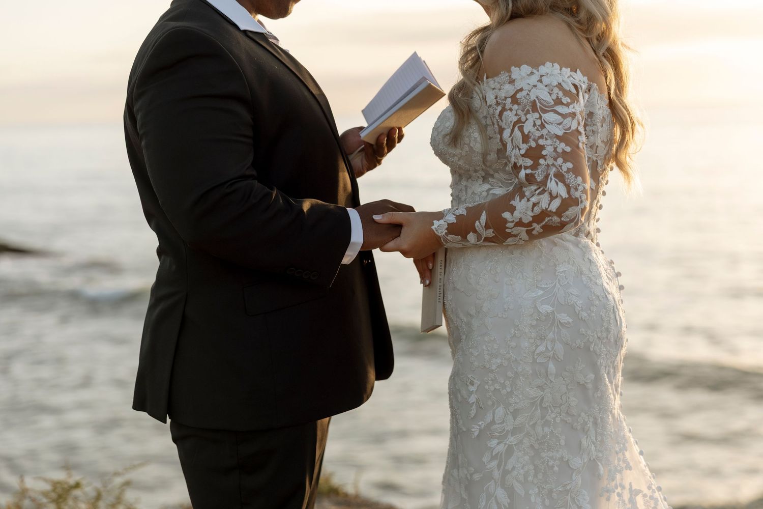 A couple in wedding attire exchanges vows during a sunset beach ceremony.