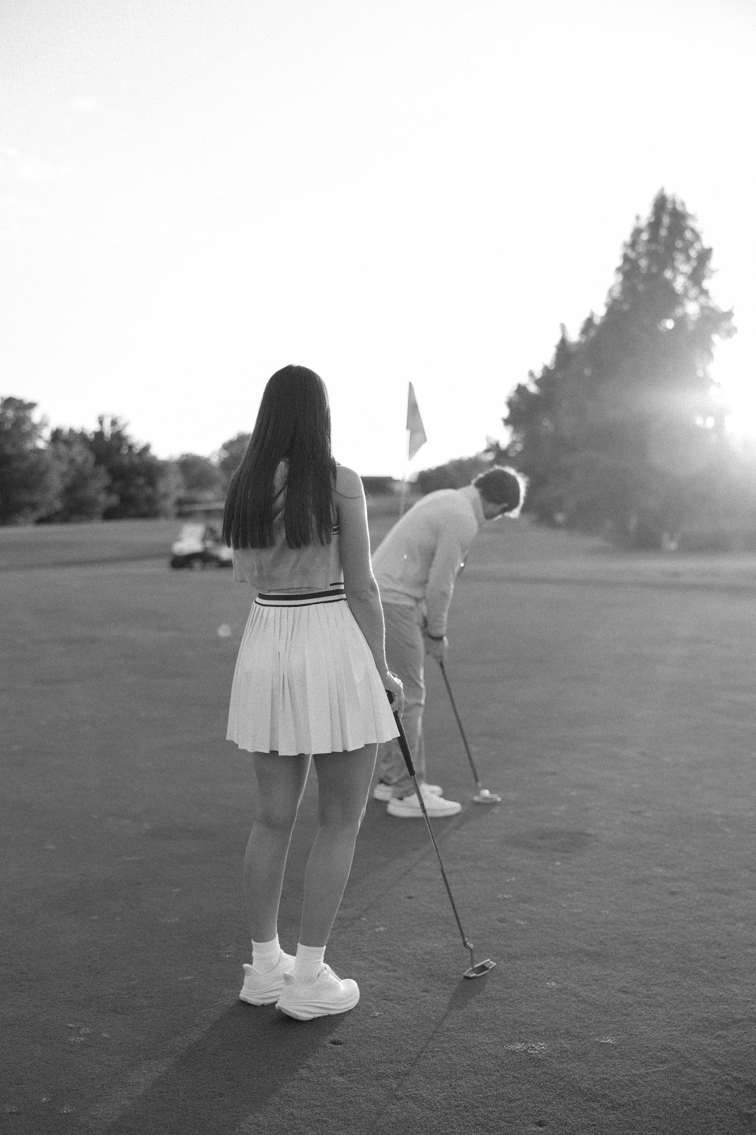 Black and white photo of golfers practicing their putting on a golf course at sunset.