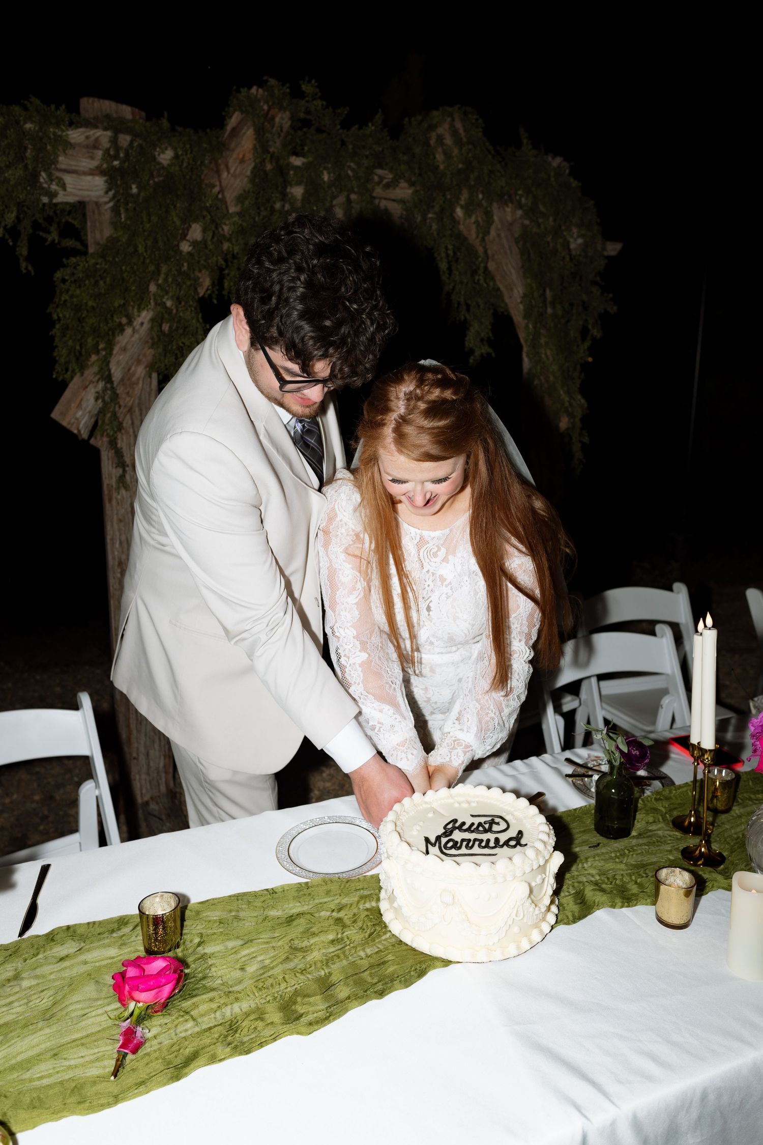 A couple cuts their white wedding cake together at their outdoor reception.
