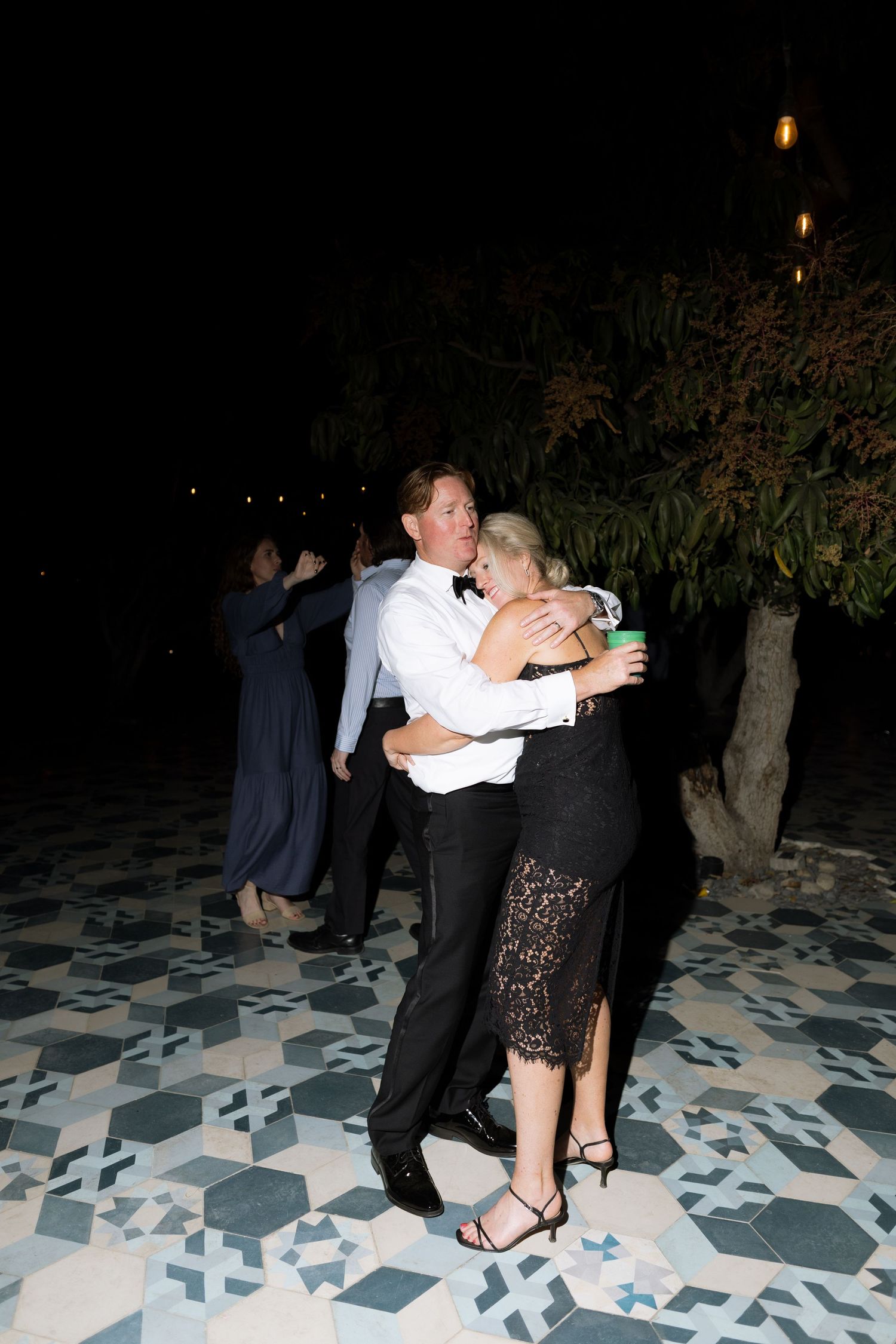 Couple dancing closely at an outdoor evening wedding reception on a patterned tile floor.