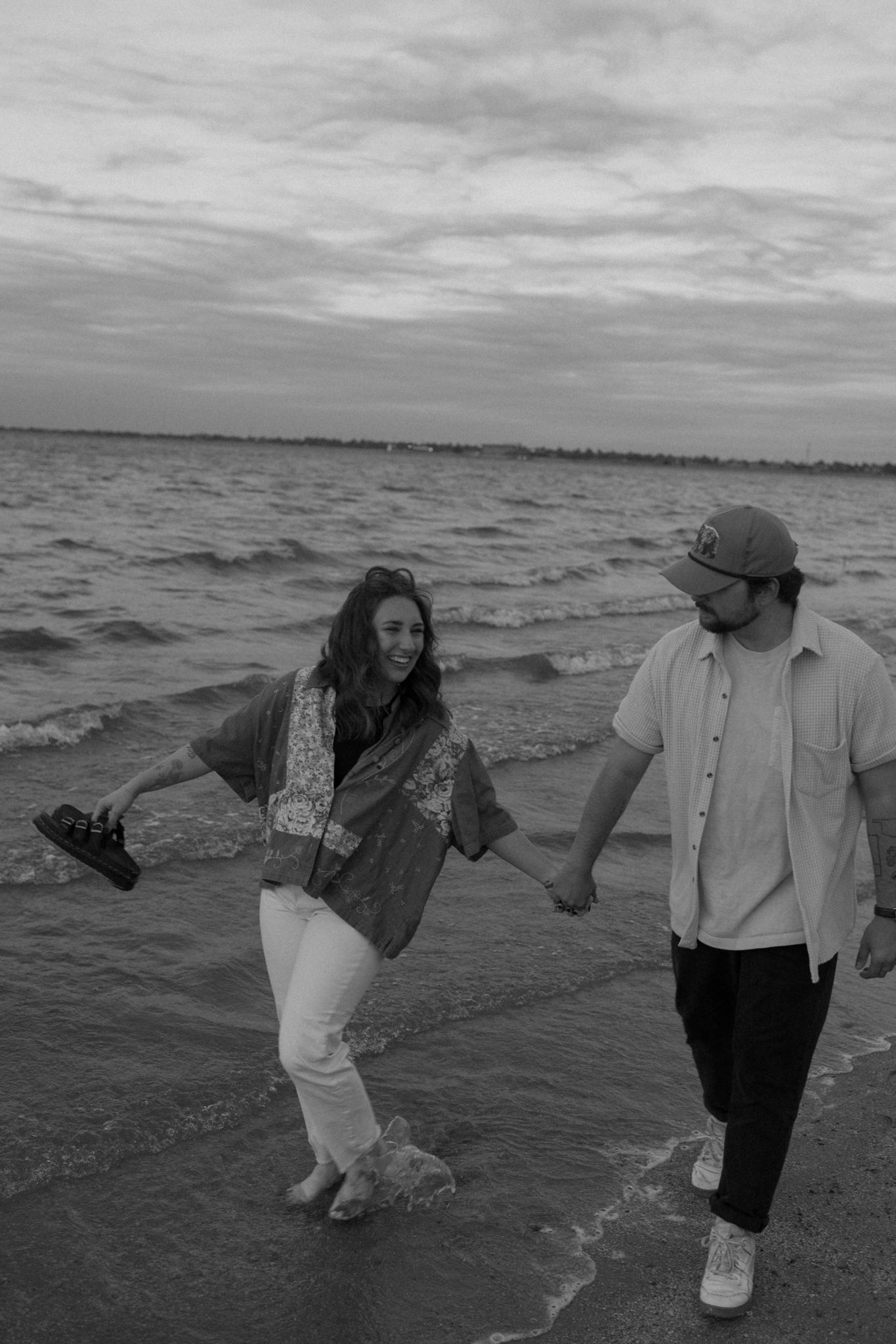 A couple holding hands while walking through gentle waves at the beach.