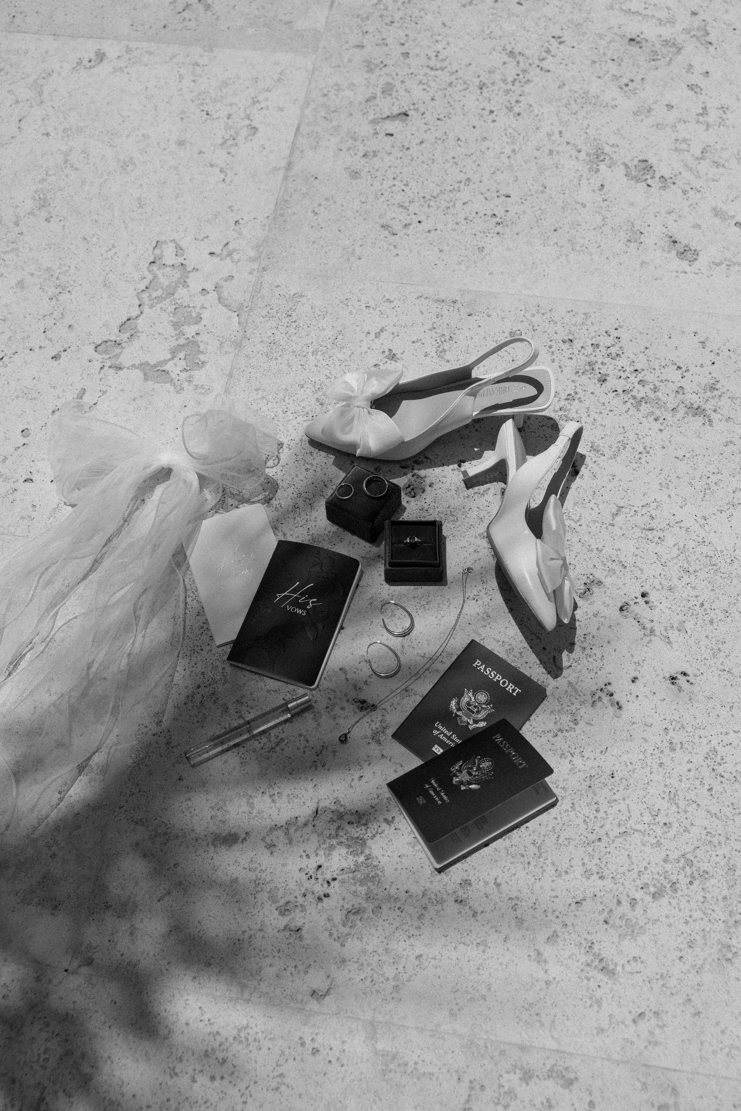 Black and white wedding details with passports and rings on textured surface.