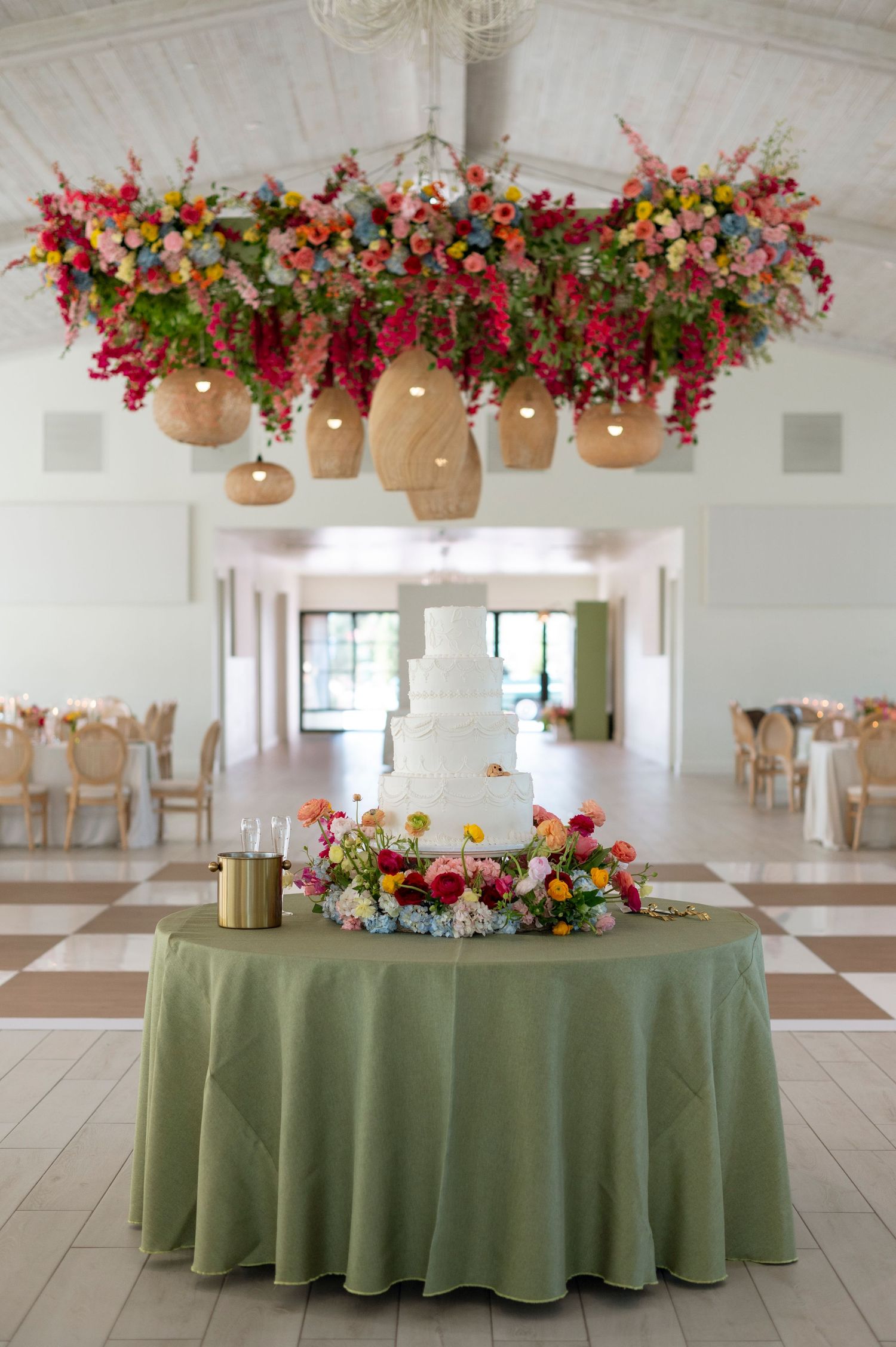 Wedding reception tables decorated with sage green linens and hanging floral arrangements in rustic brown pots.