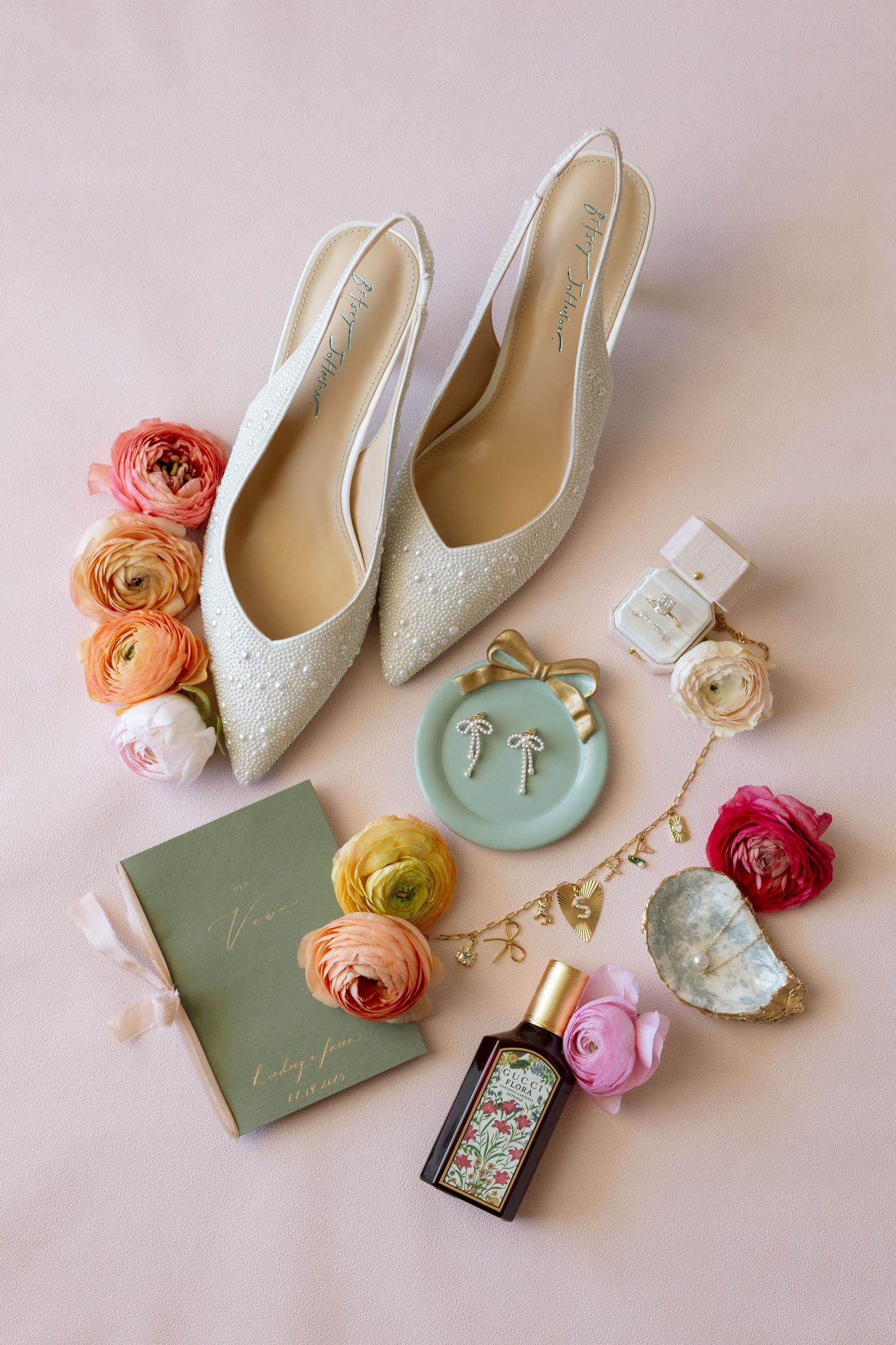 Wedding accessories including white lace shoes, colorful ranunculus flowers, and delicate details arranged on a light background.