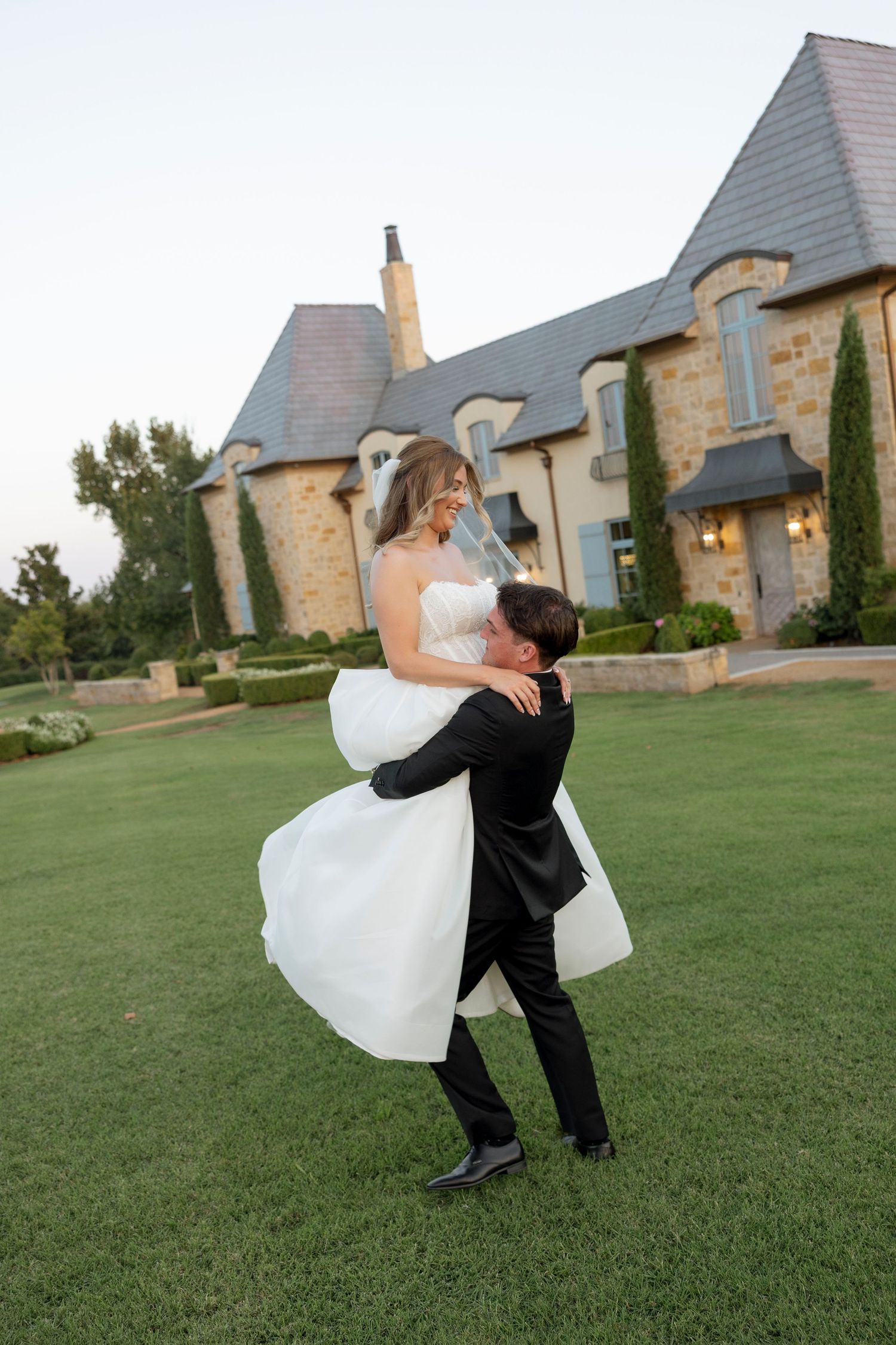 Romantic wedding couple dancing and dipping on a green lawn with a stone mansion in the background.
