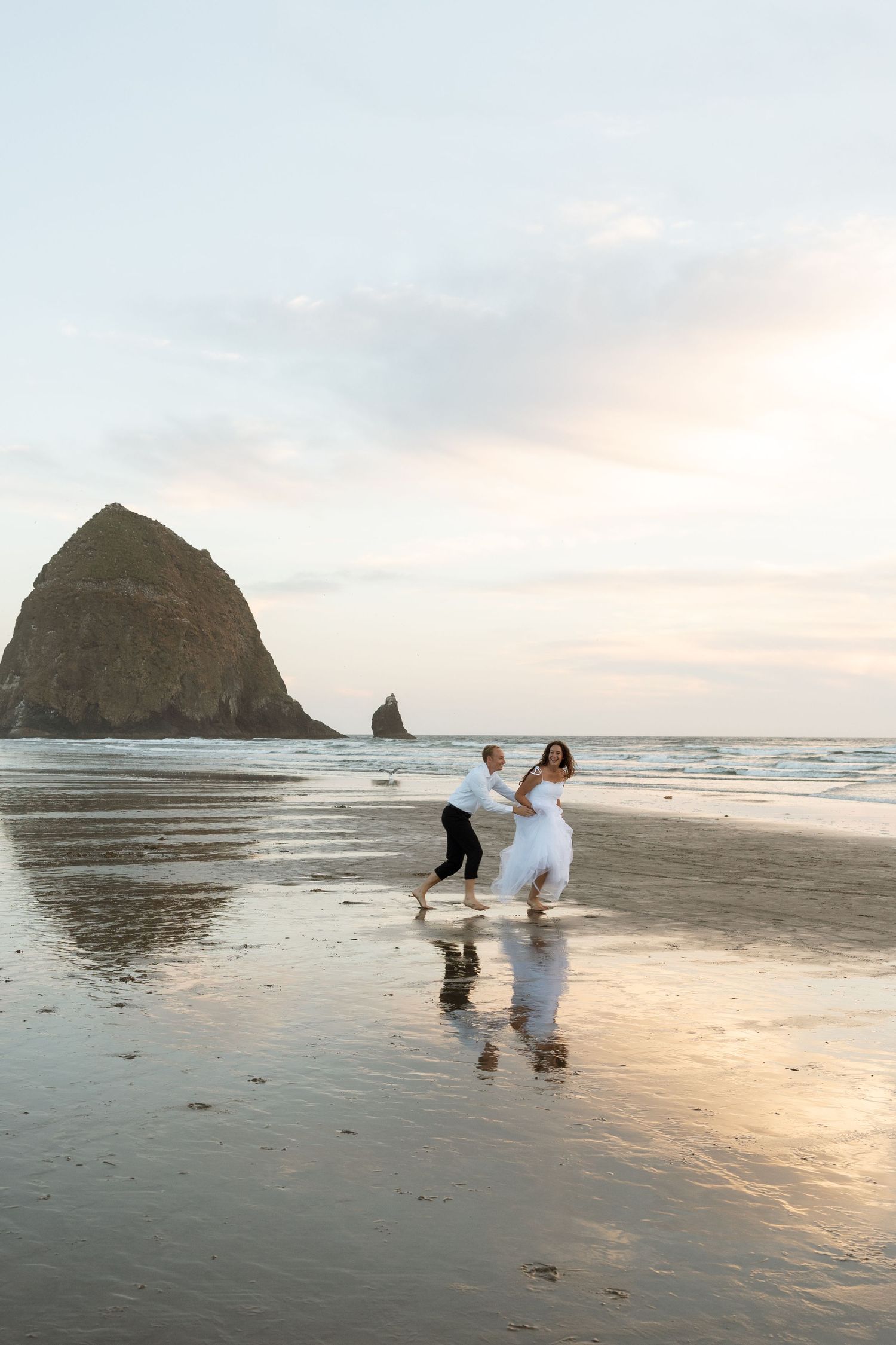 A couple dances on the wet sand of Cannon Beach with iconic Haystack Rock visible at sunset.