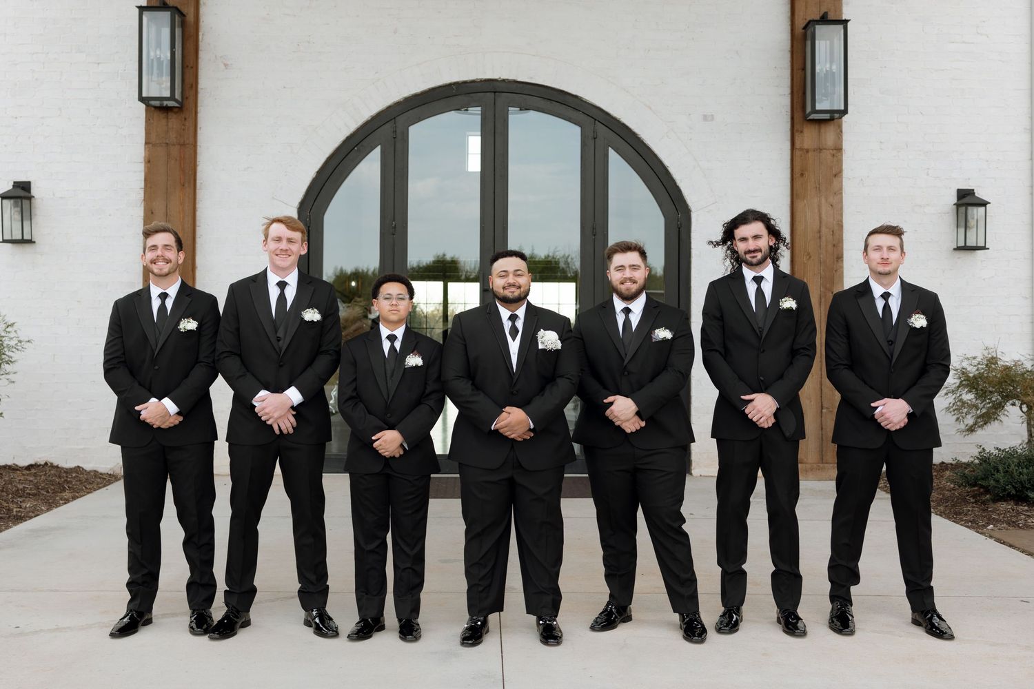 A wedding party in black suits poses in front of an arched doorway.