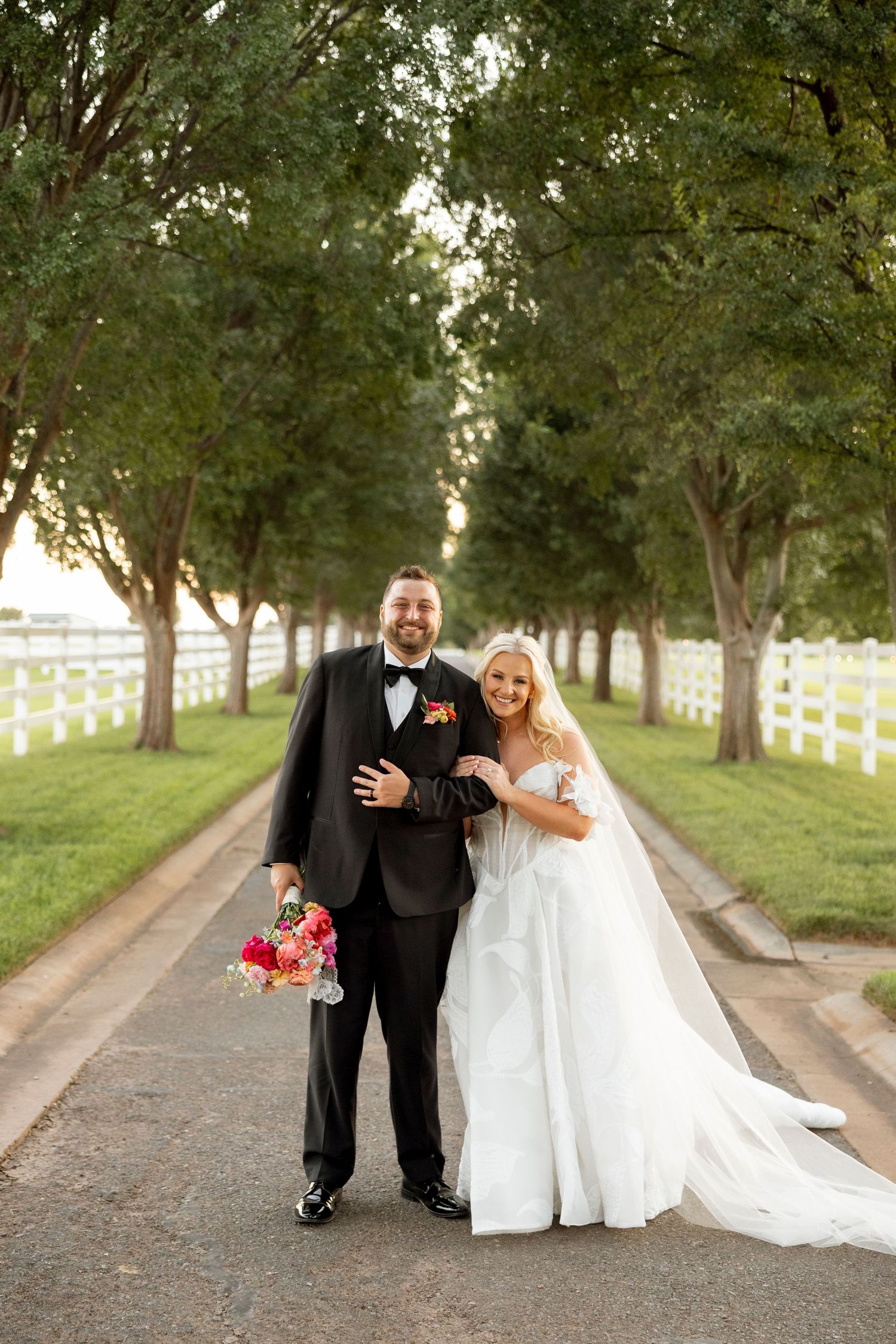 Tree-lined pathway with white fencing creates romantic setting for special occasion photography.