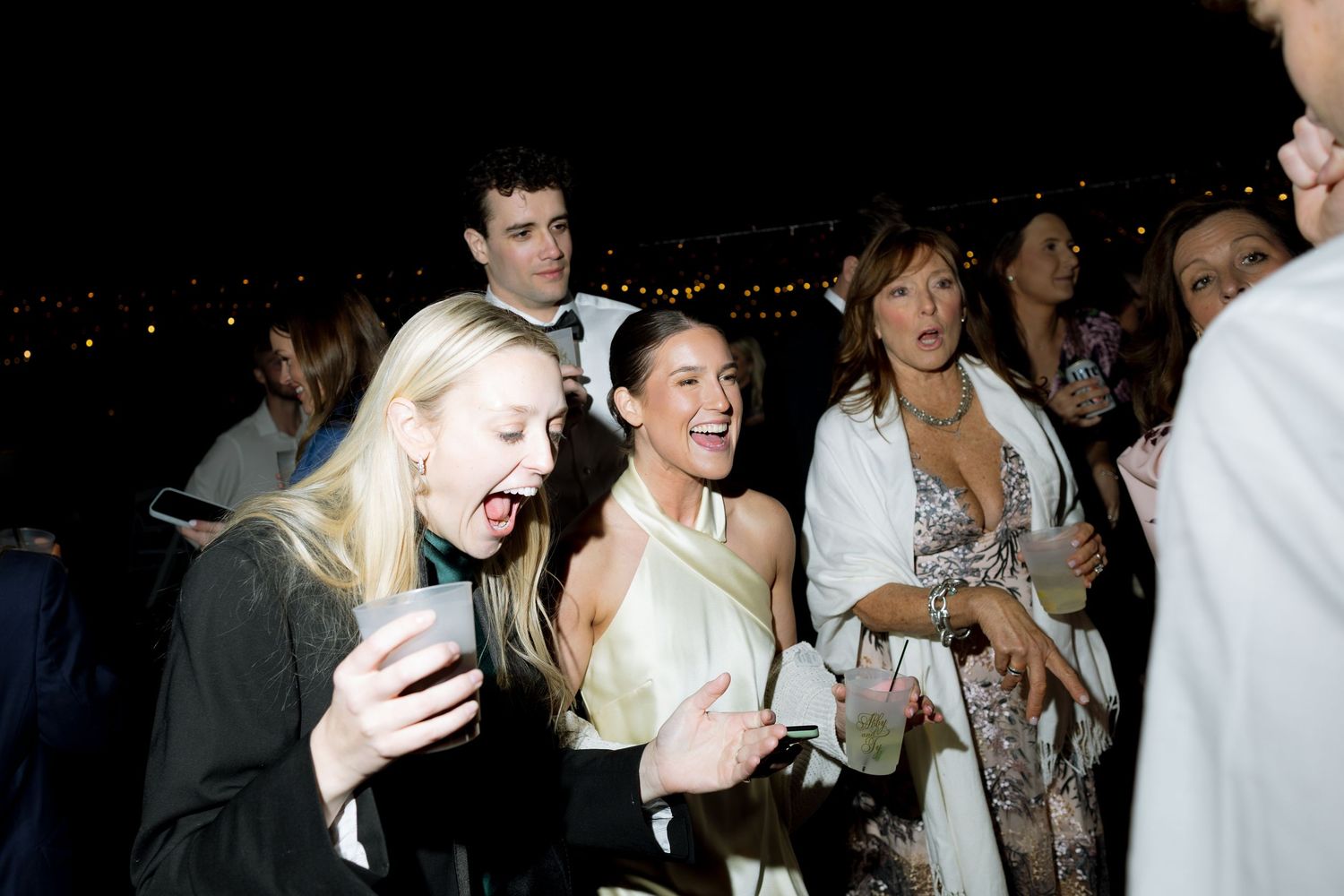 Excited wedding guests laughing and celebrating together during lively outdoor evening reception party.