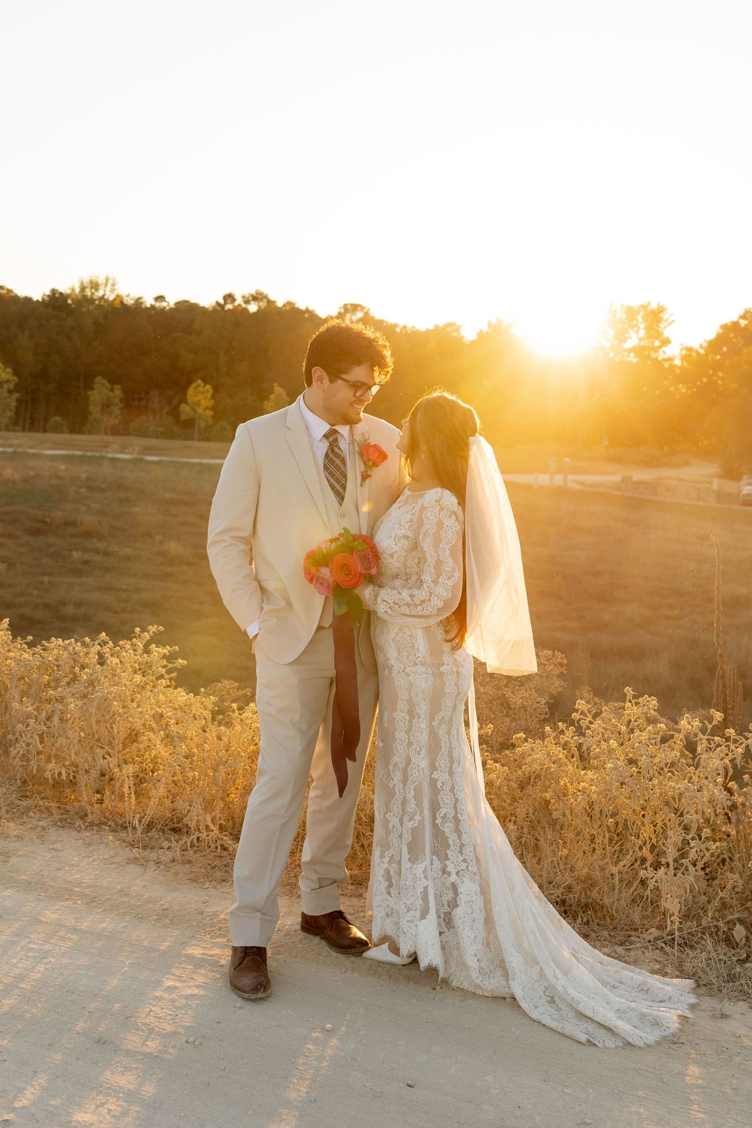 A romantic golden hour wedding portrait with the couple in elegant attire against the setting sun.