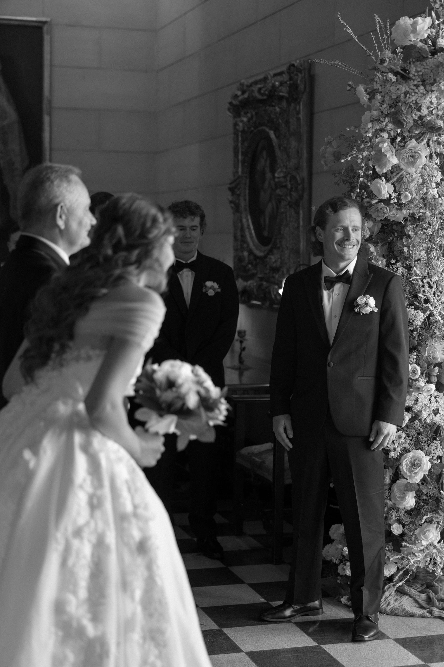 Black and white photo of a wedding ceremony in an elegant venue with floral arrangements.