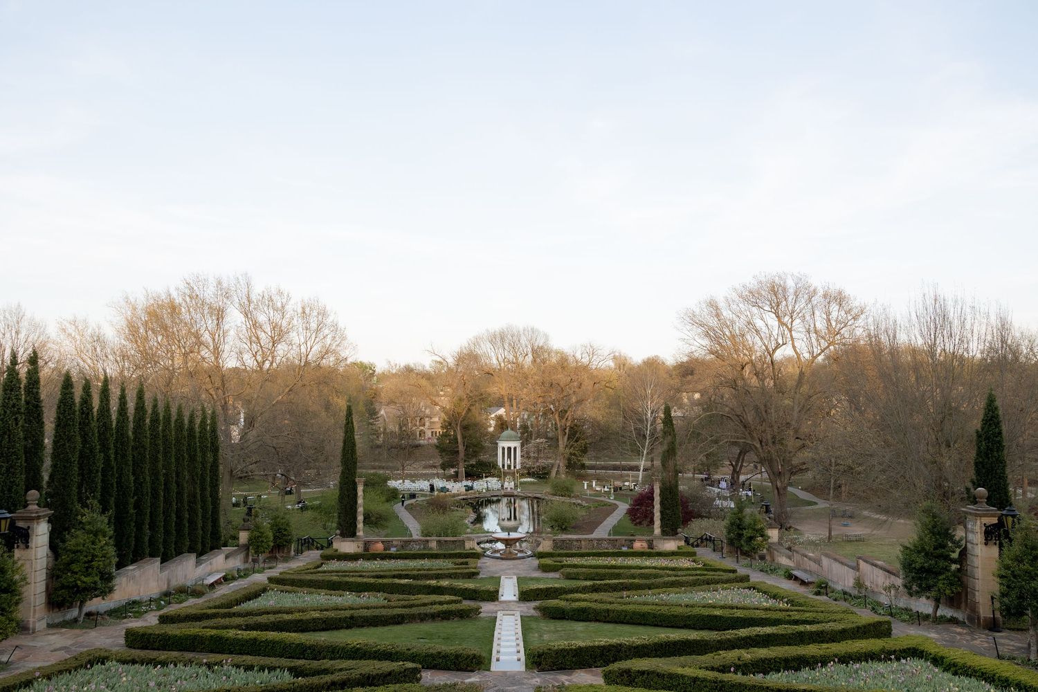 Formal garden with symmetrical hedgerows, cypress trees, and fountain at golden hour in a scenic outdoor venue.