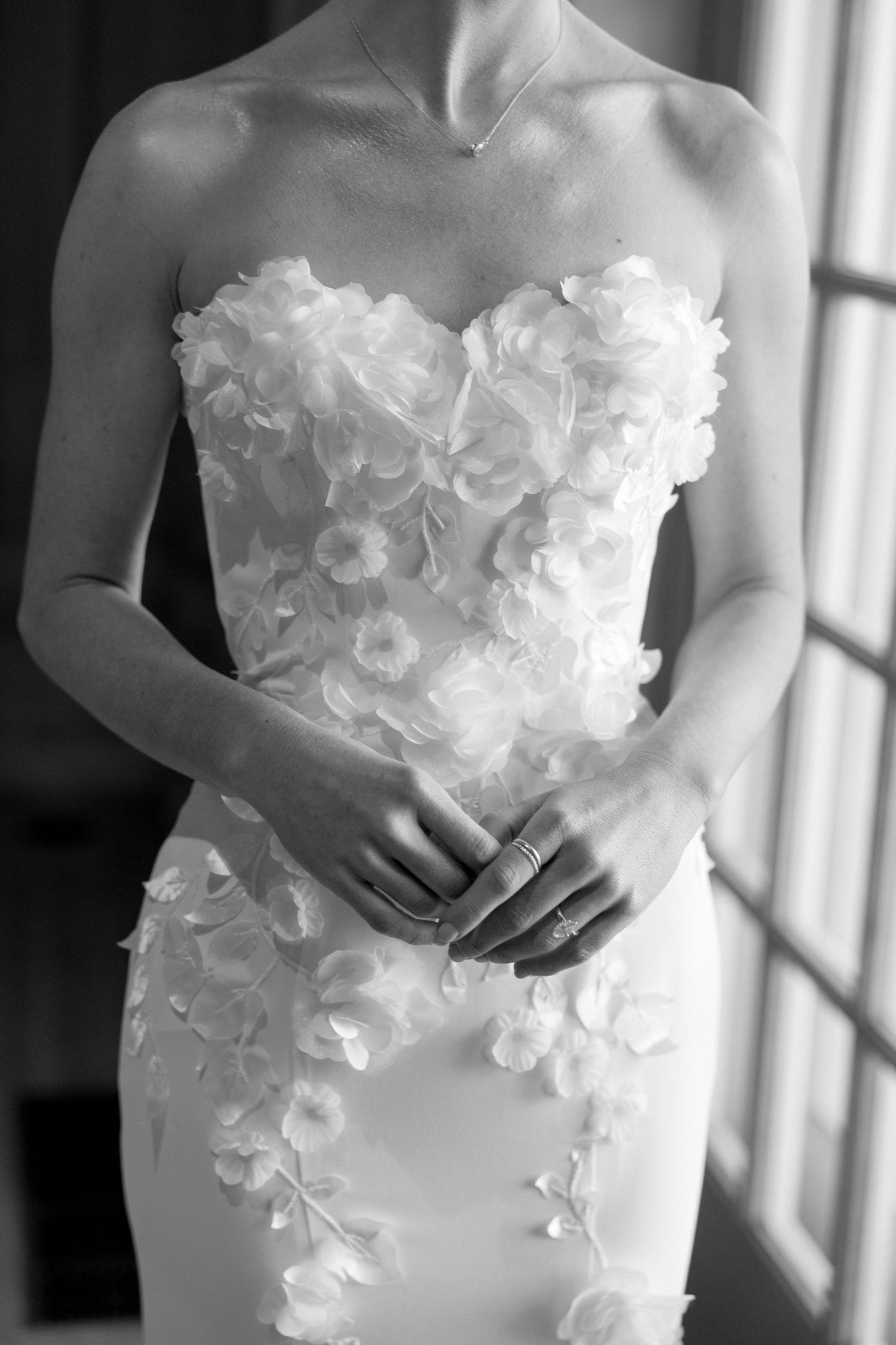 Black and white close-up of bride in strapless floral applique wedding gown with rings on hands.