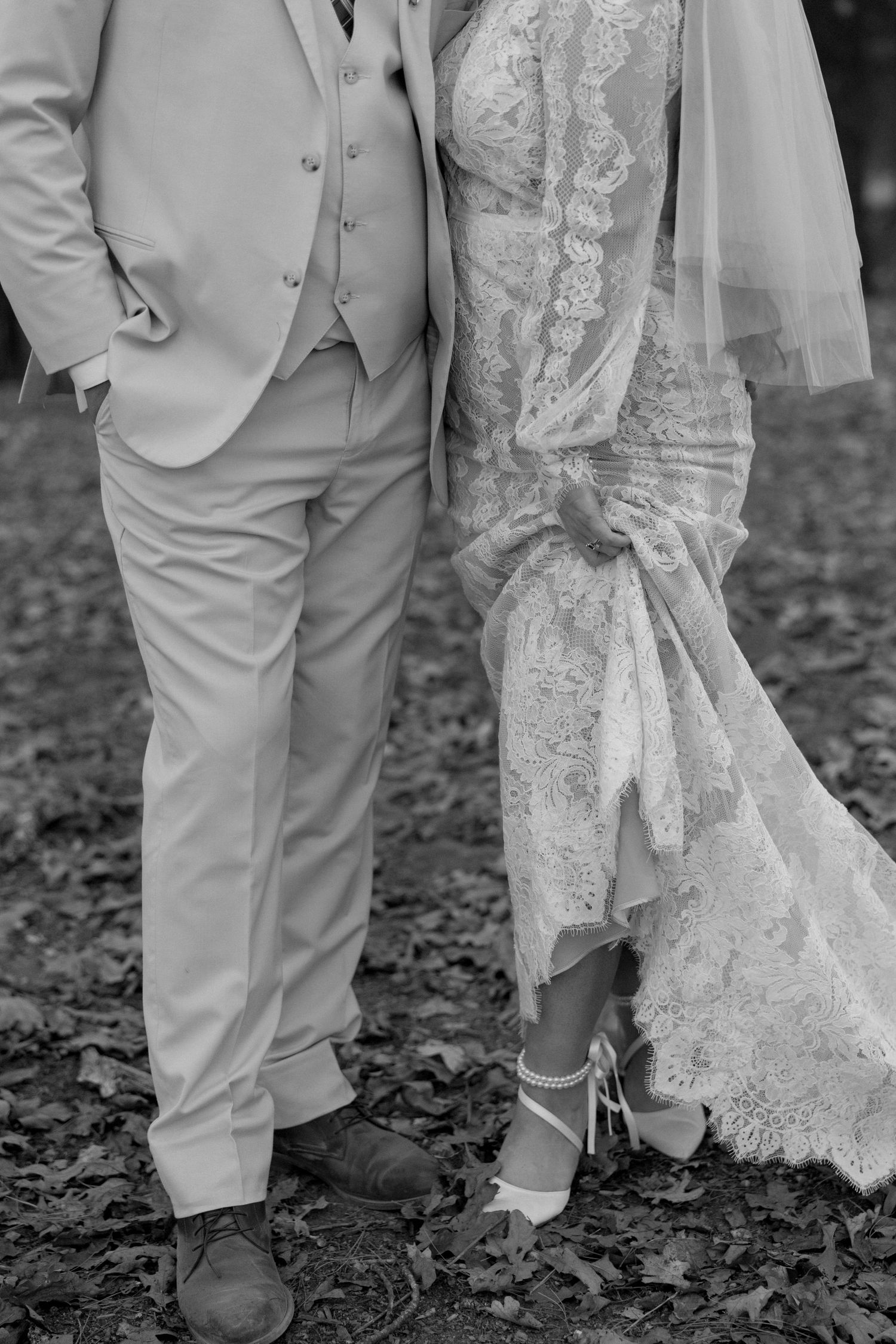 Black and white detail shot of bride and groom's attire showing elegant dress and light-colored suit.