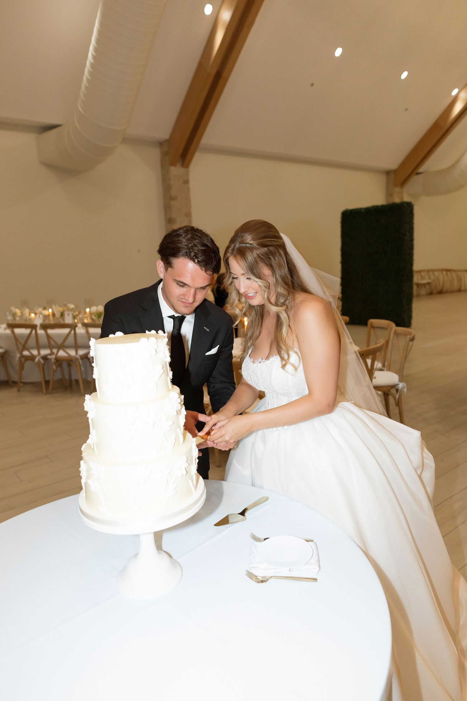 Newlyweds cutting their elegant white wedding cake together in reception venue.