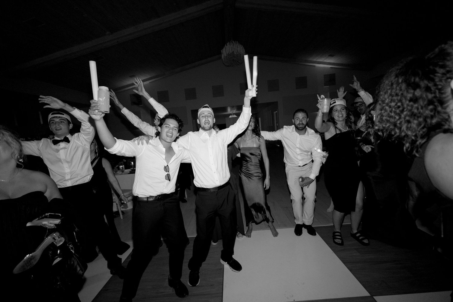 Black and white photo of wedding guests dancing in celebration on the dance floor.