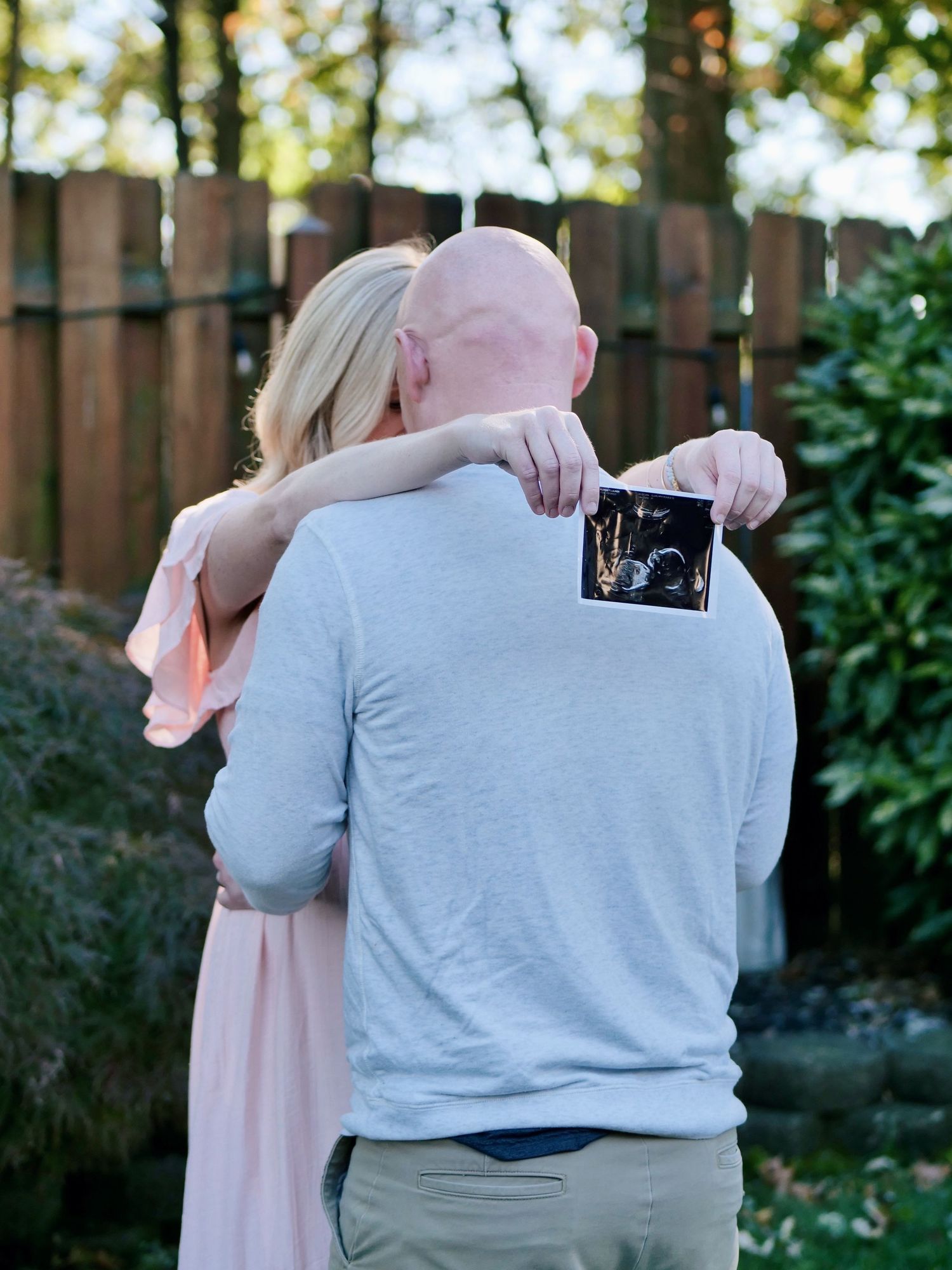 Couple kissing while holding ultrasound photo in a backyard pregnancy announcement.