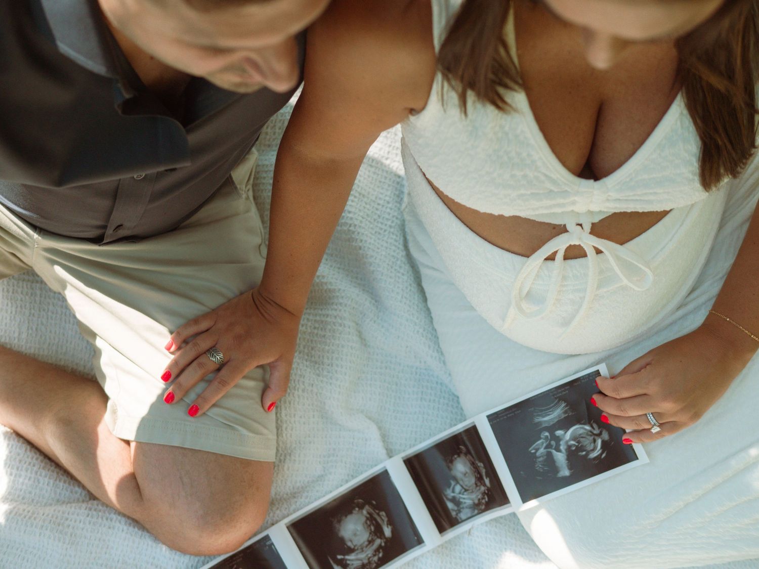 Expecting couple reviews baby ultrasound photos together during outdoor maternity photoshoot.