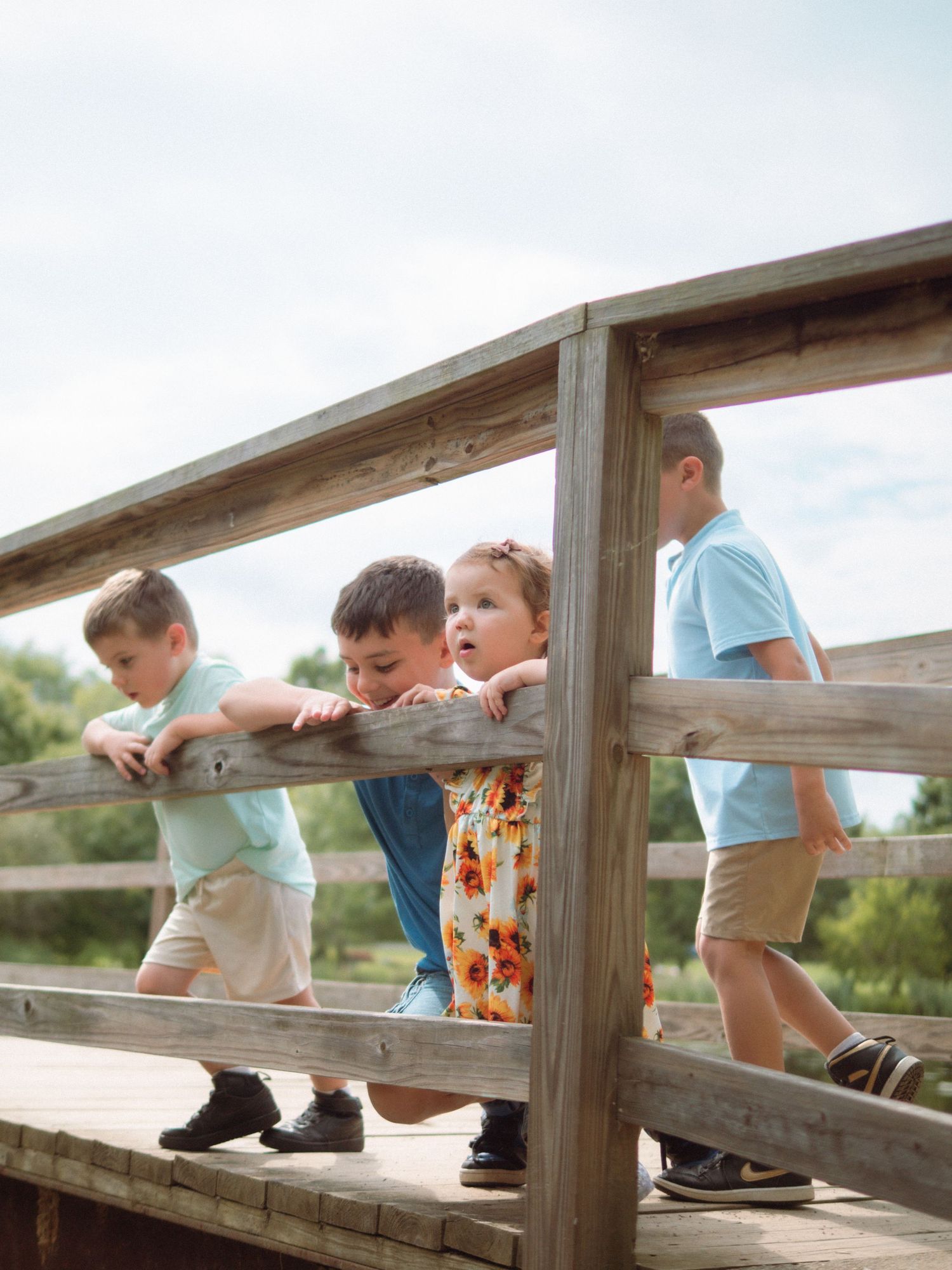 Four children lean over wooden bridge railing, exploring nature on a sunny day.