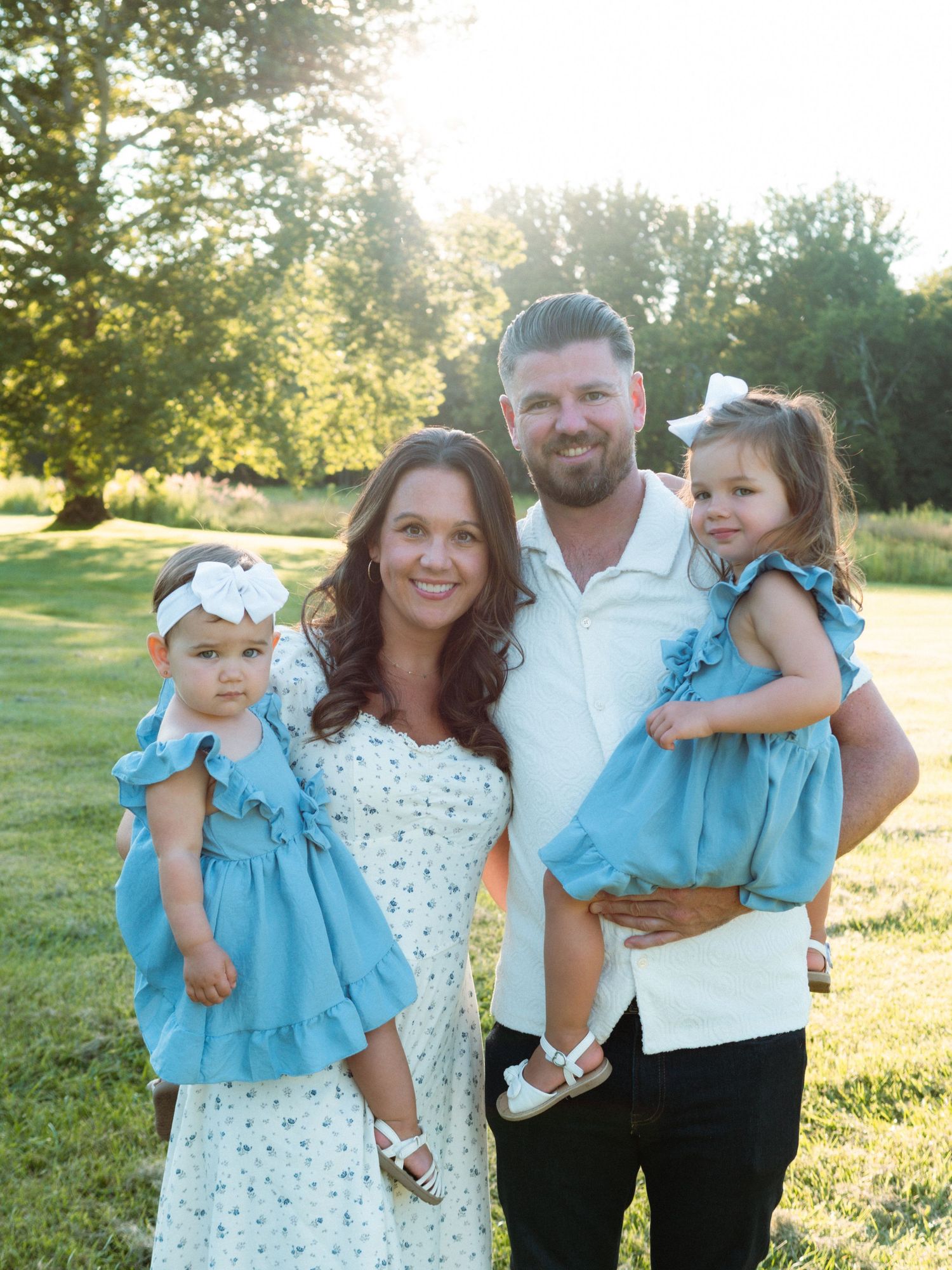 A joyful family of four poses in matching outfits in a sunlit green park.